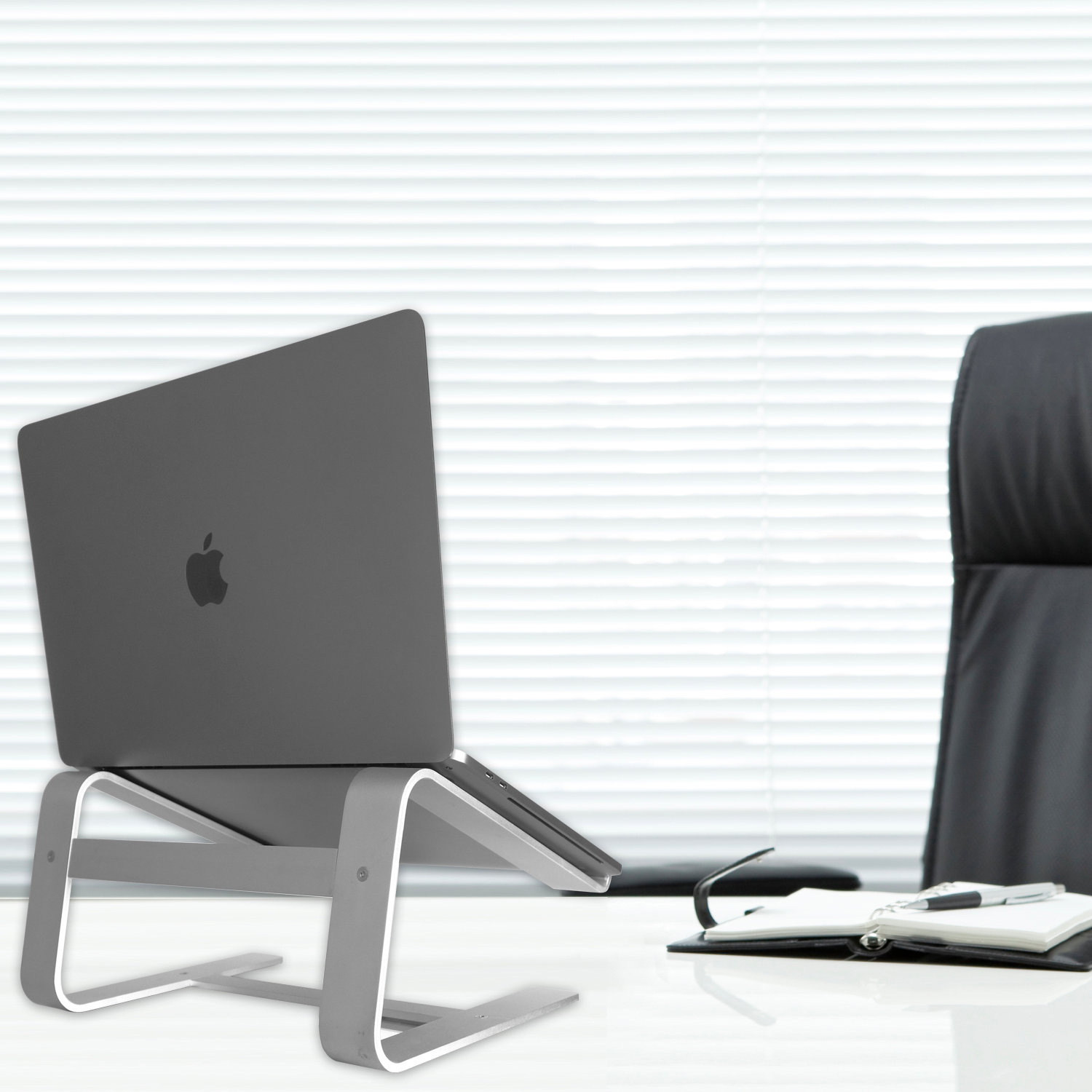 Laptop grigio su un supporto, sedia e tavolo neri in ufficio.