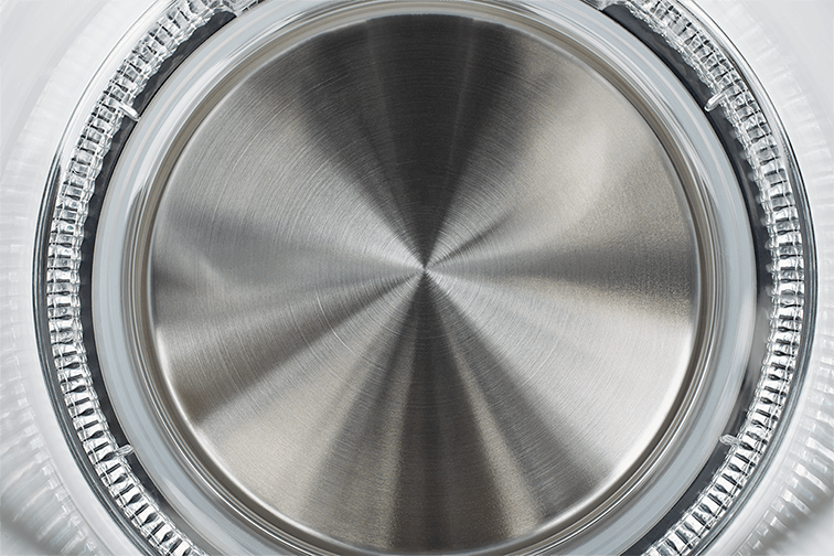 Zbliżenie podstawy stalowego czajnika z okrągłym, szczotkowanym wzorem metalu.