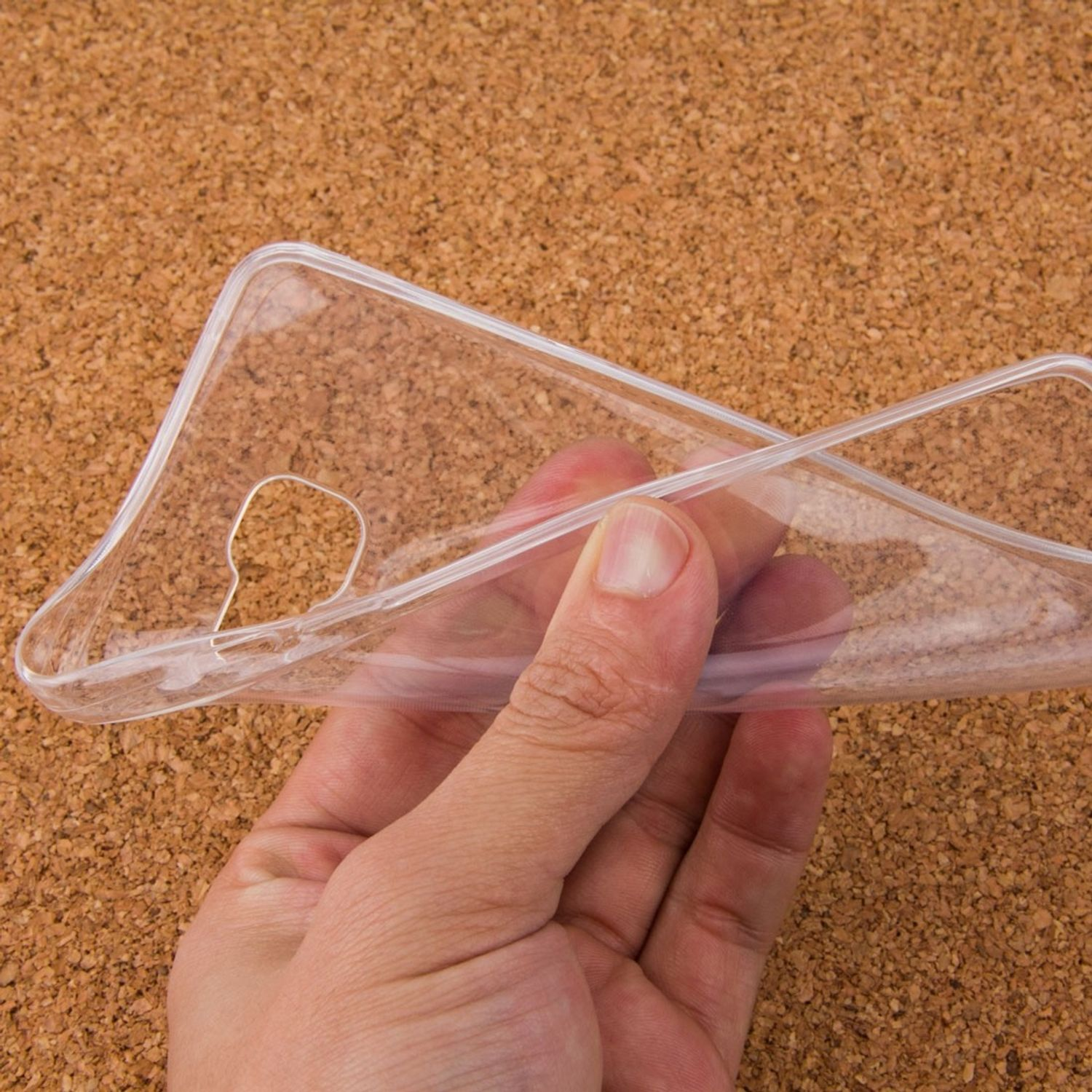 Eine transparente Handyhülle wird in einer Hand gehalten. Der Hintergrund ist Kork.