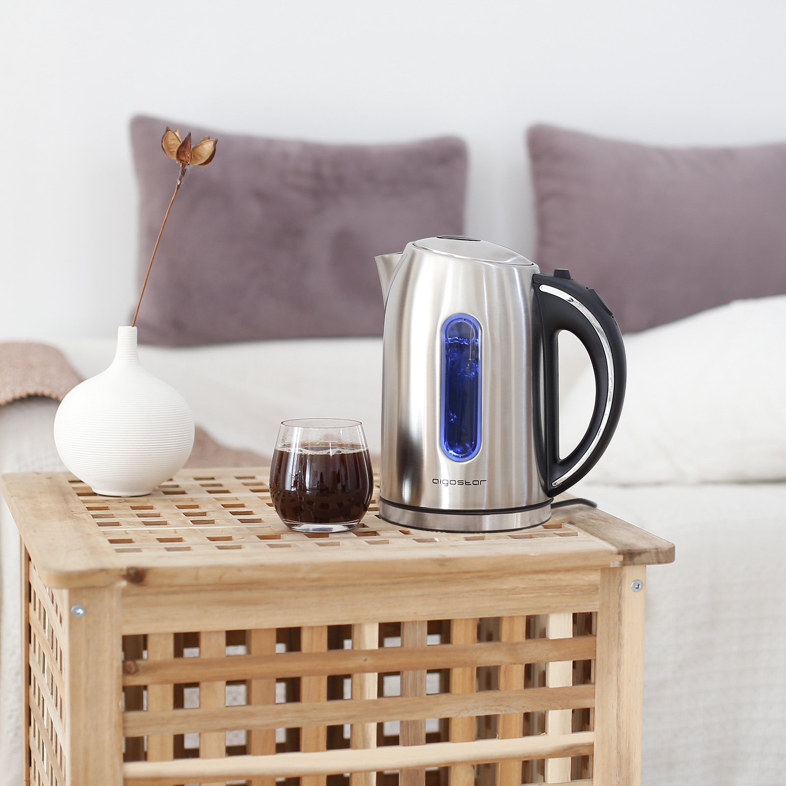 Un bollitore su un tavolo di legno accanto a un bicchiere di caffè e un vaso bianco.