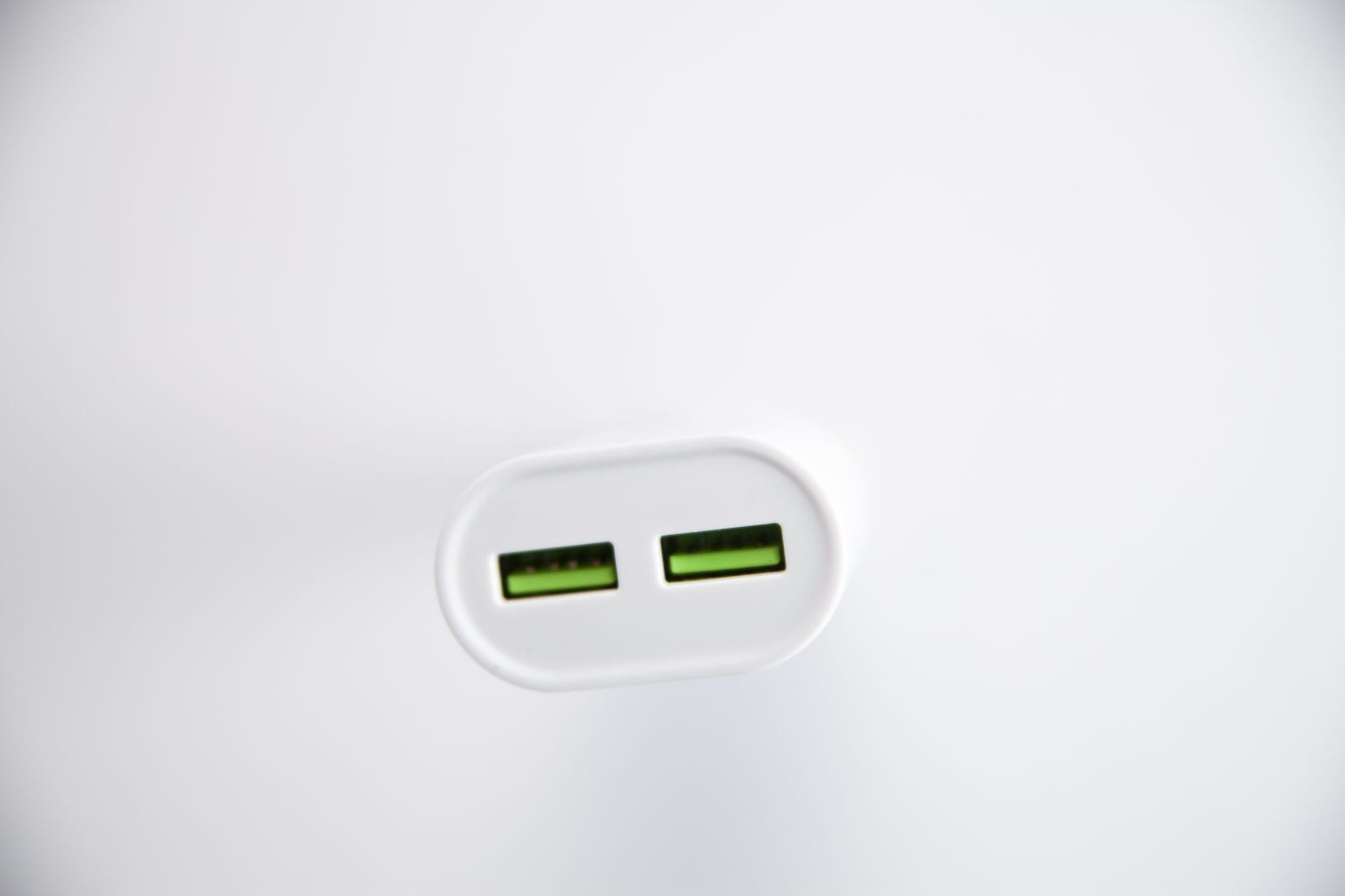Weißes USB-Ladegerät mit zwei grünen USB-Anschlüssen, von oben betrachtet. Der Hintergrund ist weiß.