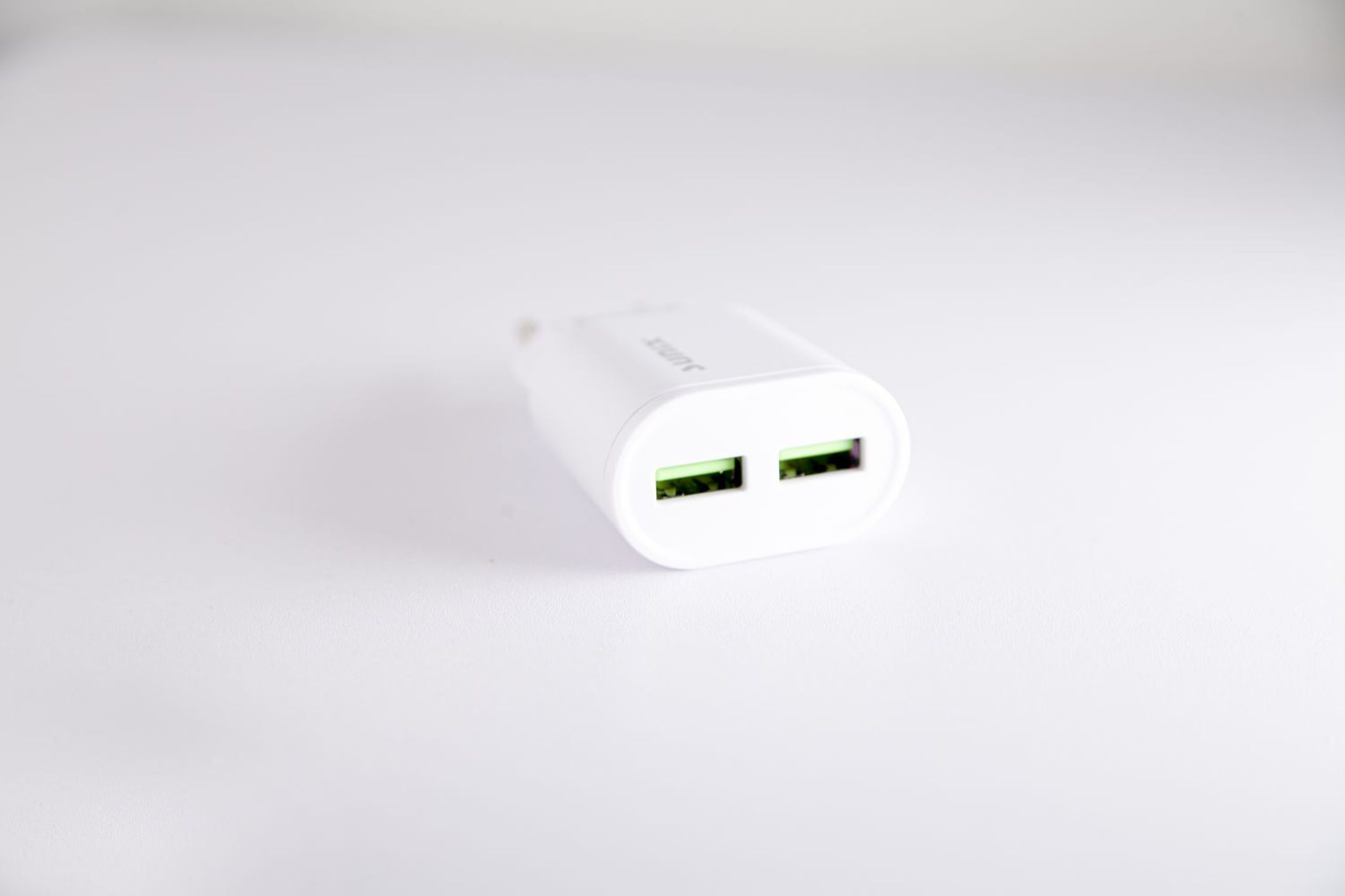 Weißes USB-Ladegerät mit zwei grünen USB-Anschlüssen. Auf weißem Hintergrund.