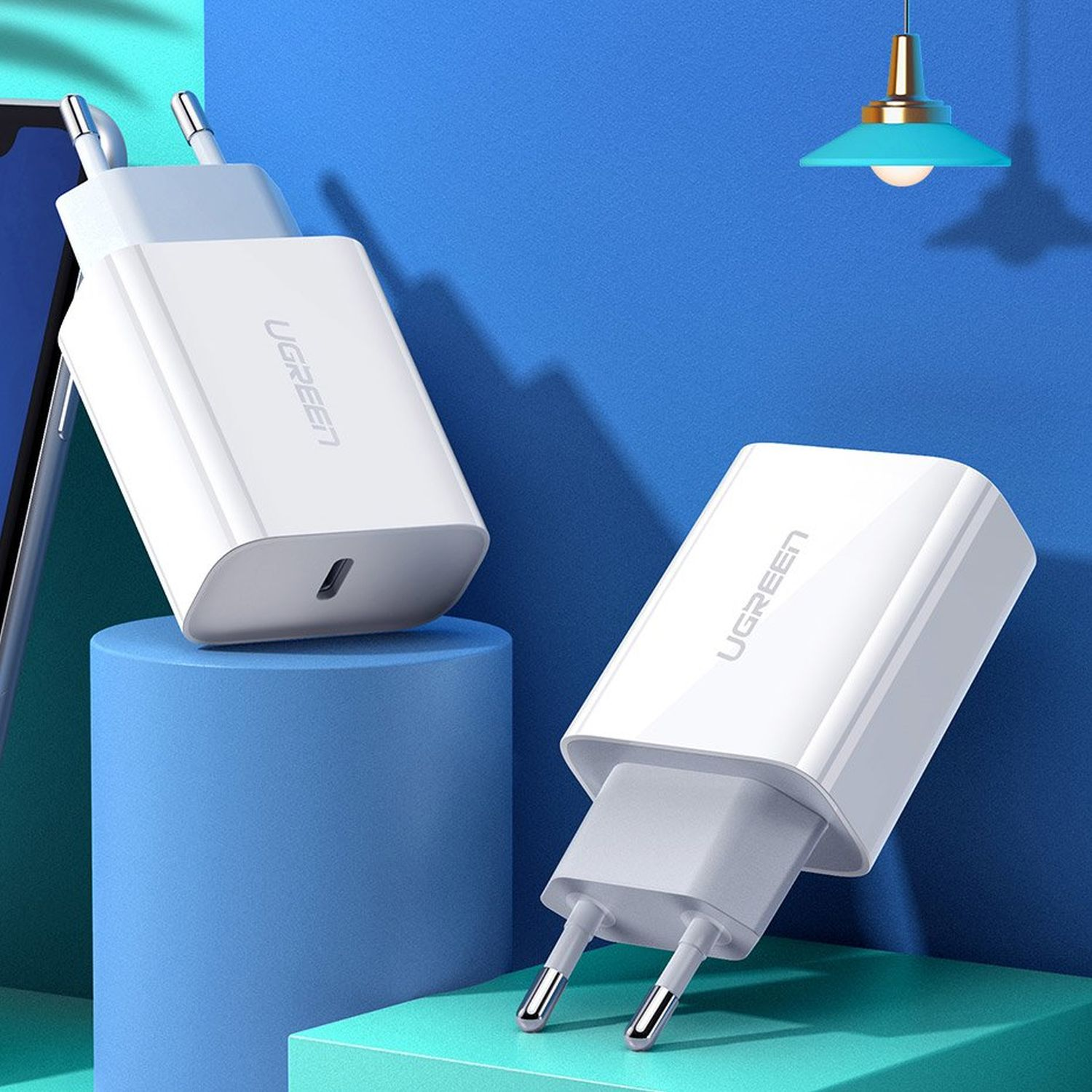 Weiße UGREEN-Ladegeräte mit USB-C-Anschluss. Zwei Ladegeräte. Eines eingesteckt. Blauer und hellblauer Hintergrund.