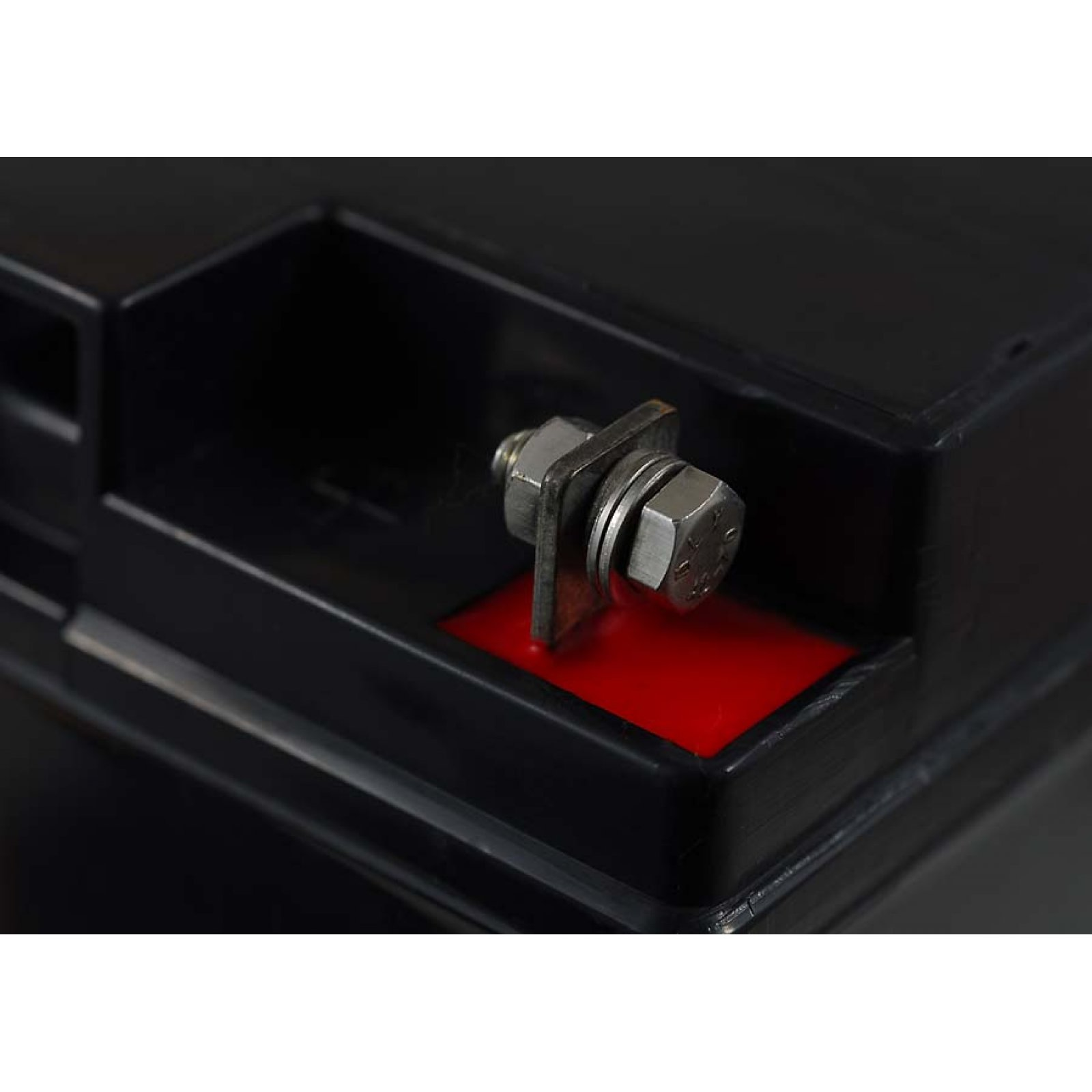 Primer plano de un terminal de batería negro con un perno, arandela y acento rojo. El fondo es negro.