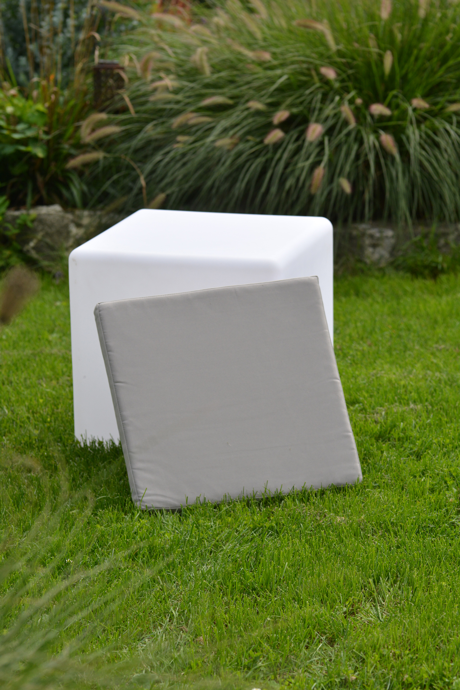 Weißer Würfel mit grauem quadratischem Kissen auf Gras.