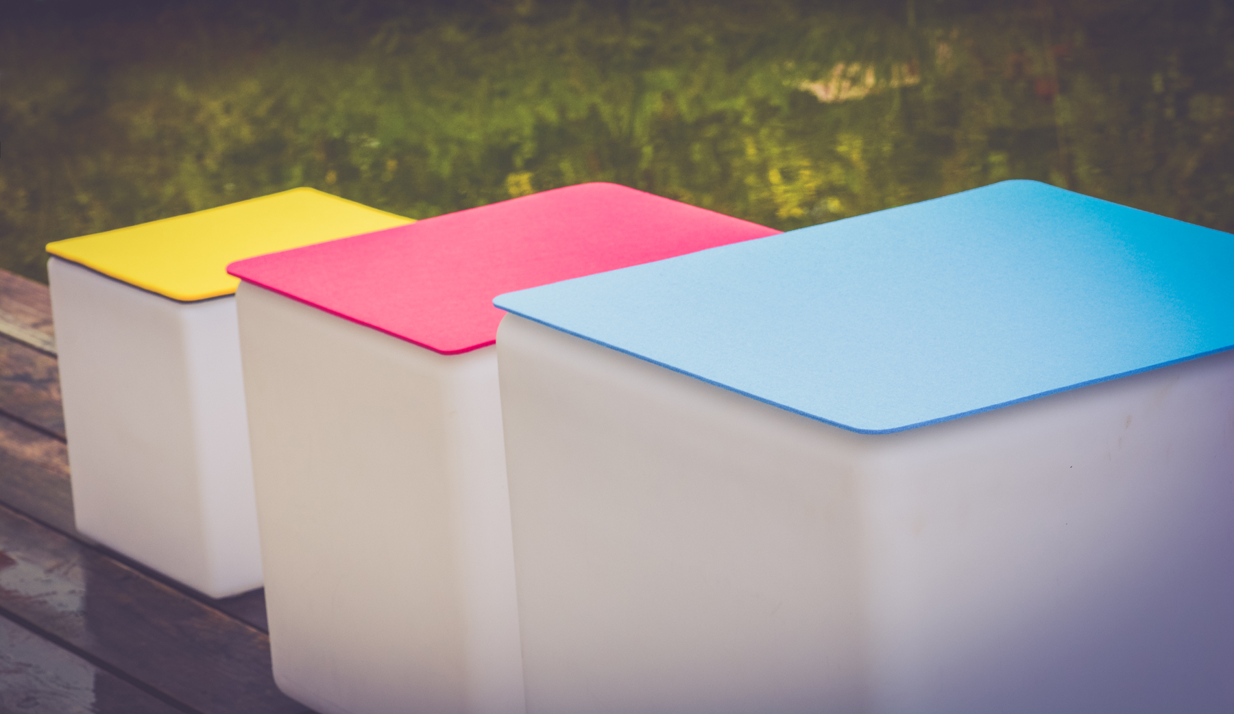 Drei weiße quadratische Aufbewahrungsbehälter mit farbigen Deckeln: gelb, rosa und blau.