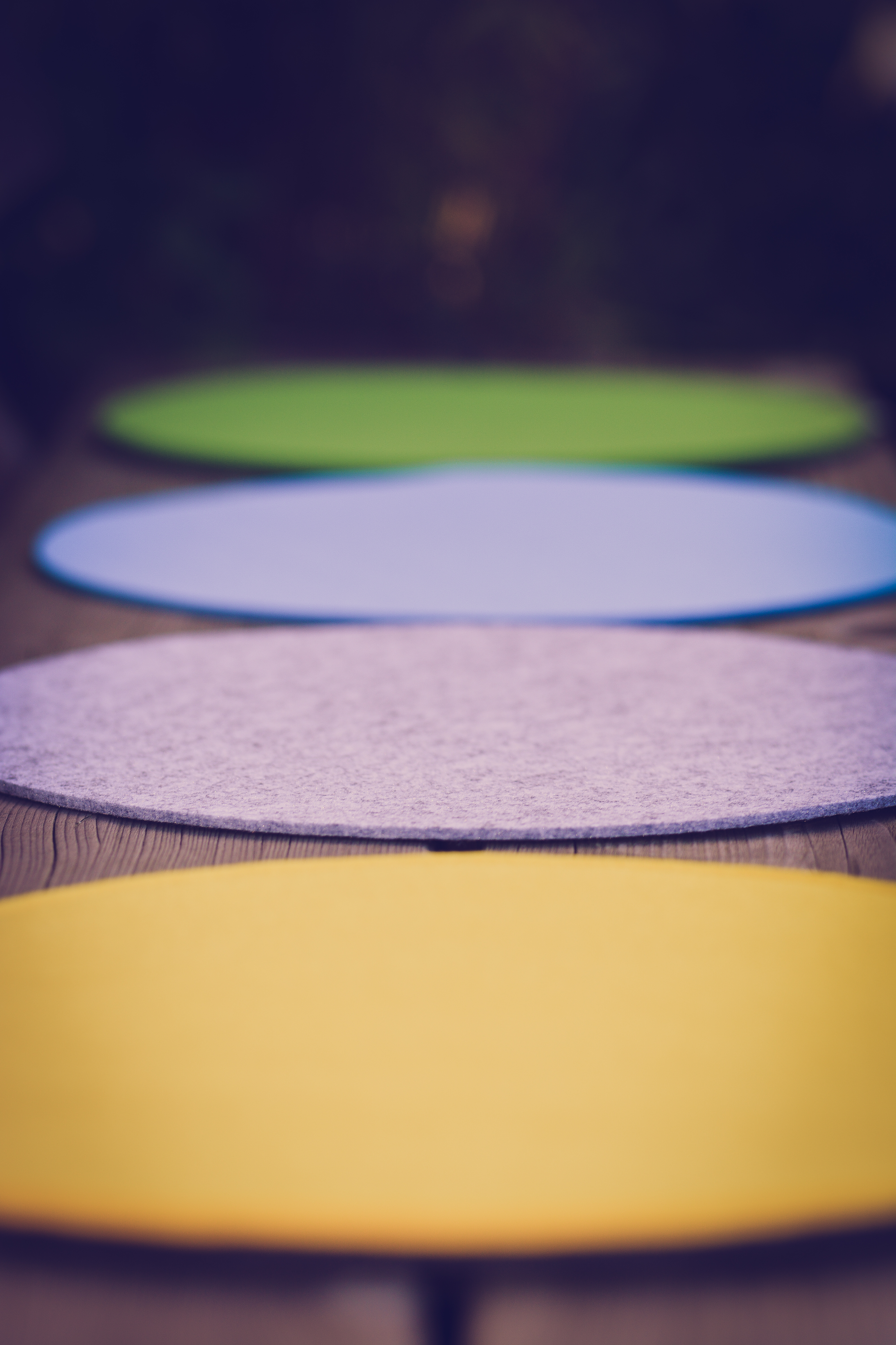 Vier farbige Tischsets, in einer Reihe angeordnet. Grün, blau, grau und gelb, auf Holzoberfläche.