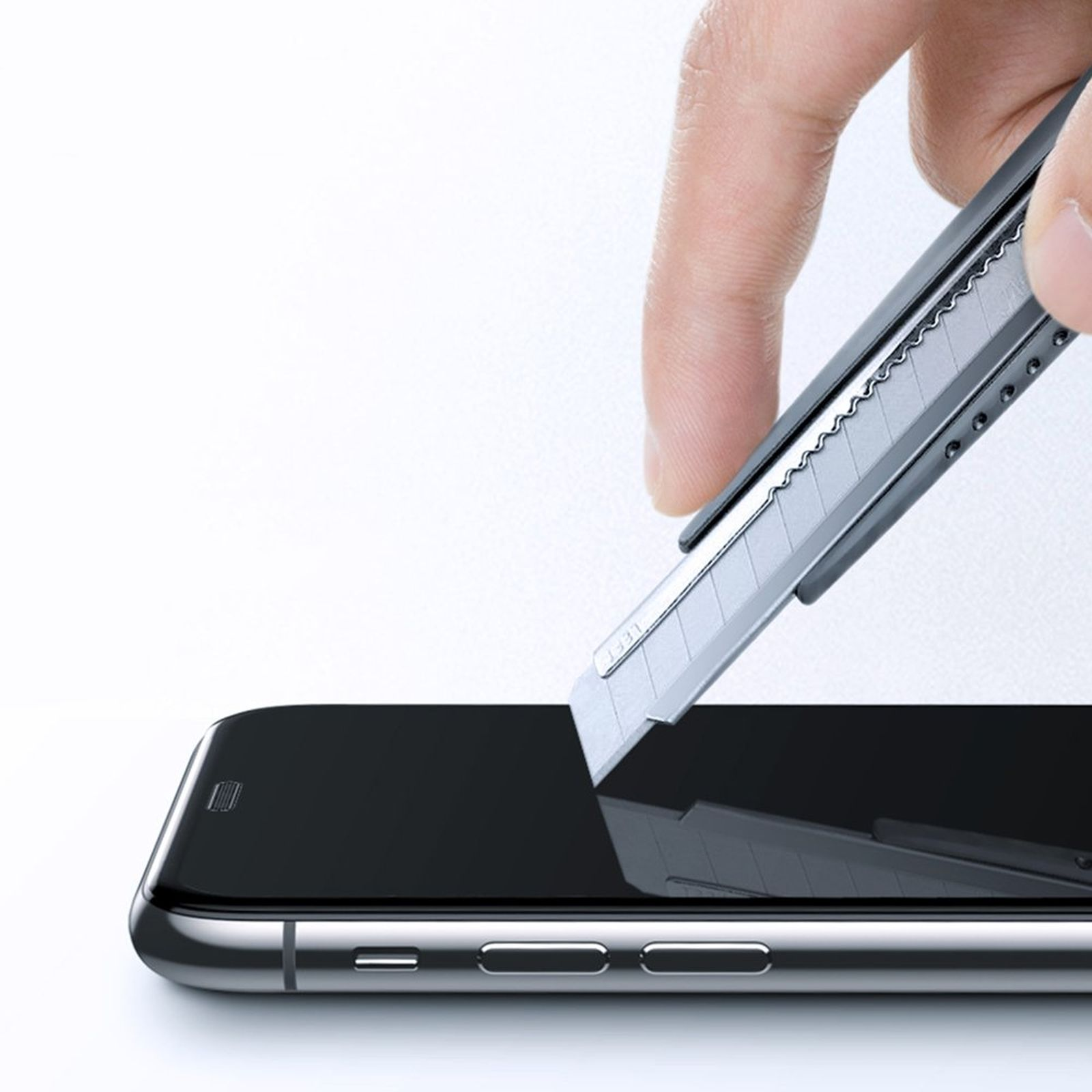 Hand, die ein Cutter verwendet, um eine Displayschutzfolie auf einem Telefon anzubringen. Weißer Hintergrund.
