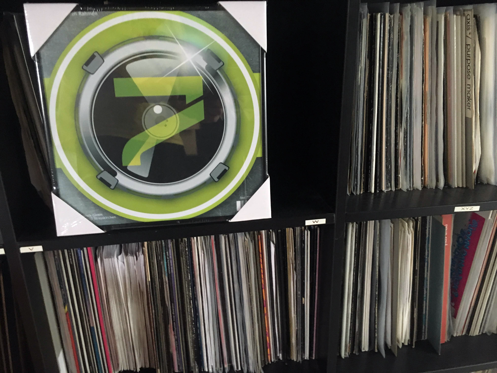 Ein gerahmtes Albumcover wird auf einem Regal mit Vinyl-Schallplatten angezeigt.