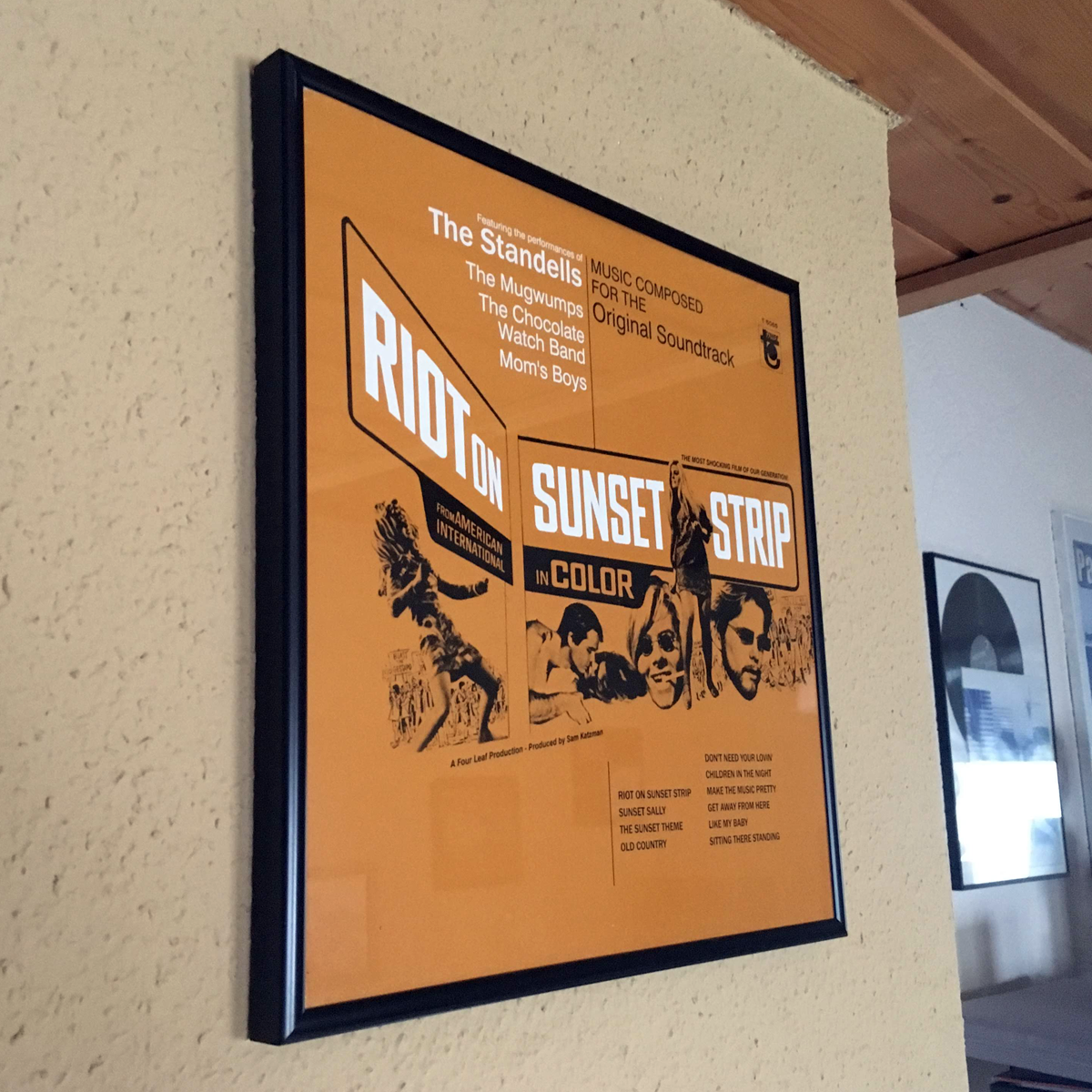 Gerahmtes Poster an einer Wand. Oranger Hintergrund, Text und Illustrationen. Schwarzer Rahmen.