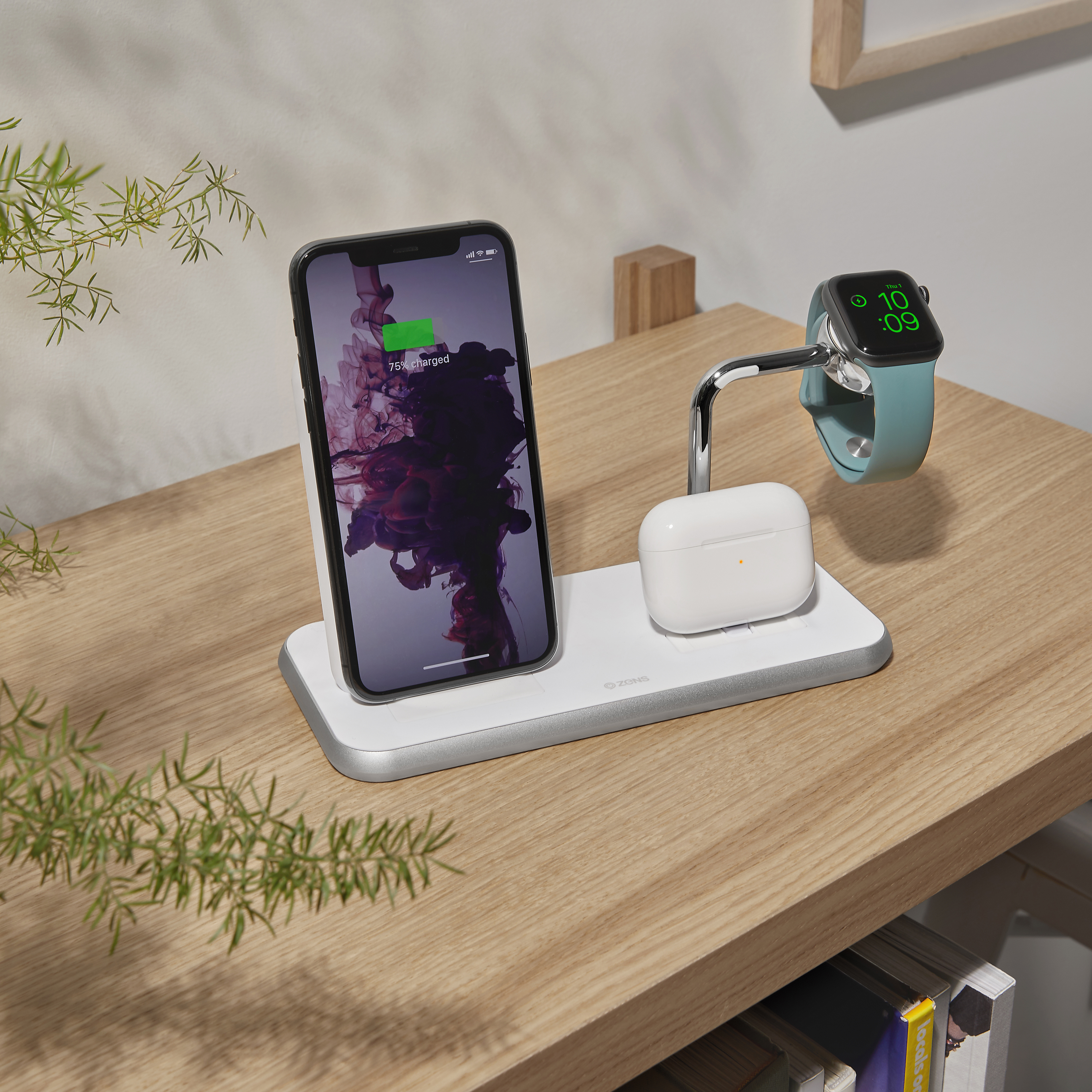 Ladestation mit Telefon, Ohrhörern und Uhr auf einem Holztisch. Links ist eine Pflanze.