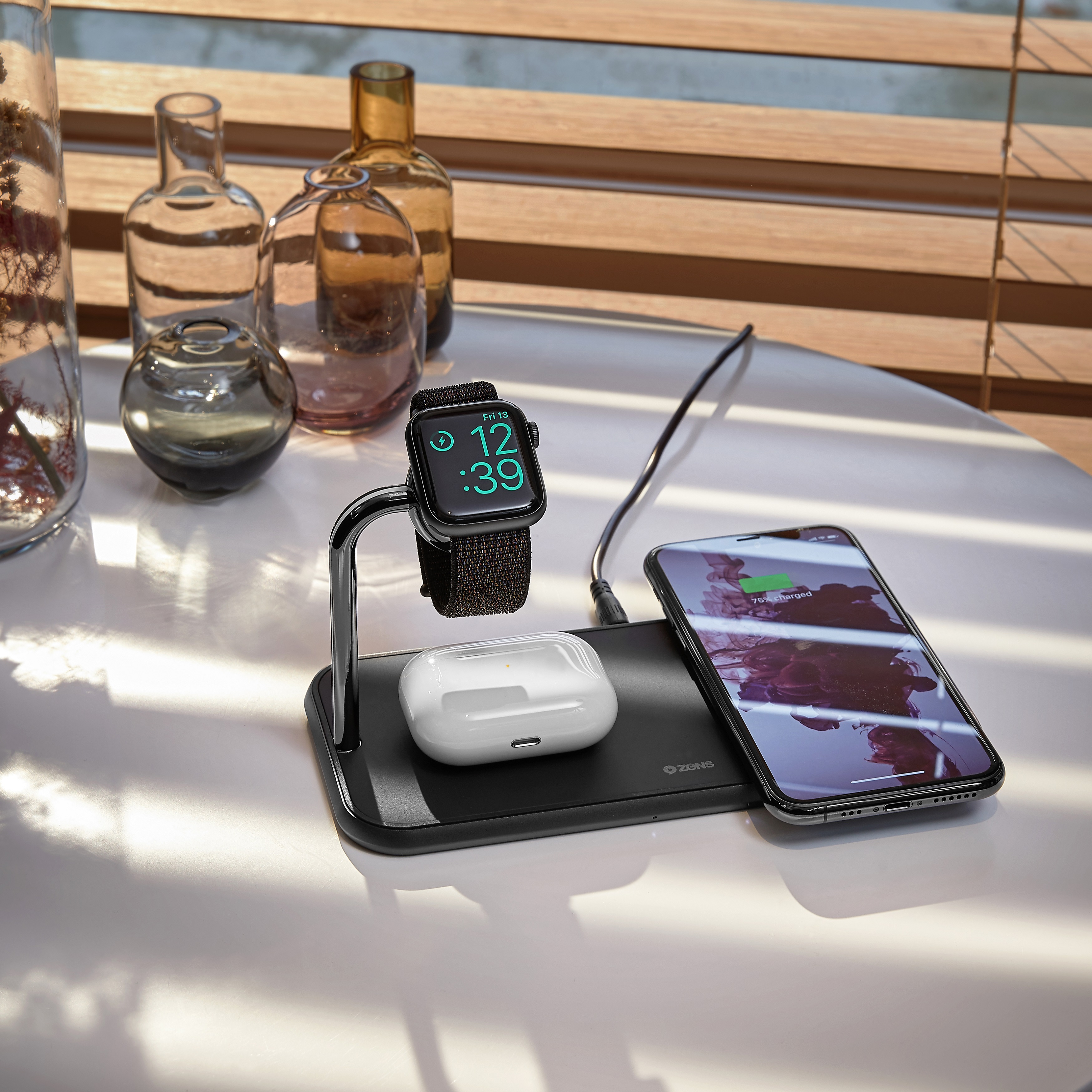 Ladestation mit Telefon, Uhr und Ohrhörern. Weißer Tisch, Glasflaschen im Hintergrund.