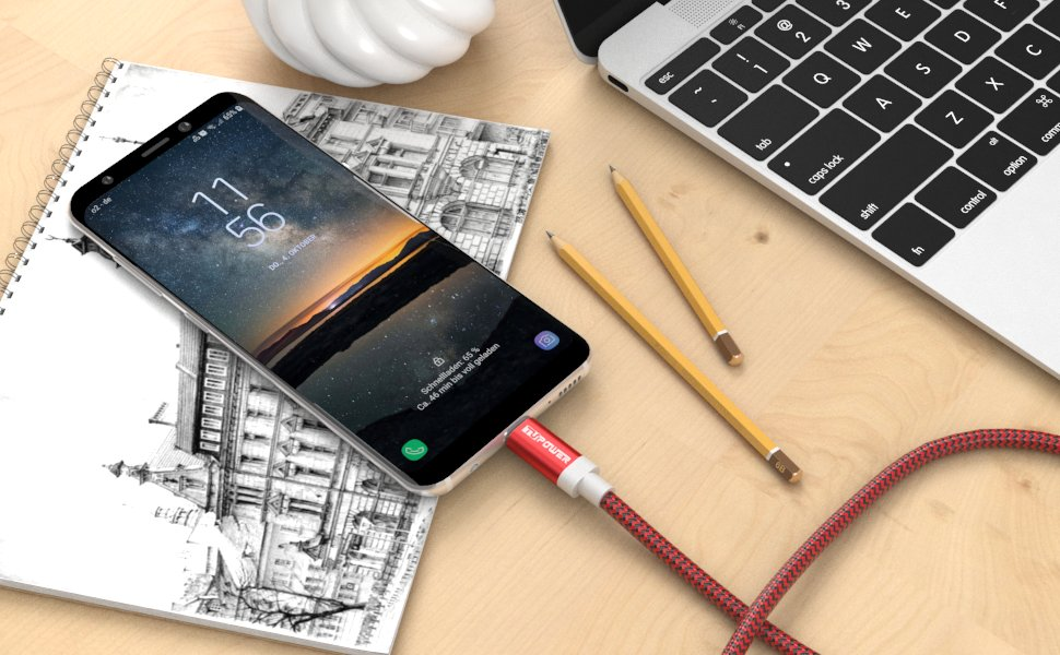 Ein Telefon wird über ein rotes Kabel auf einem Schreibtisch mit Notizbuch geladen.