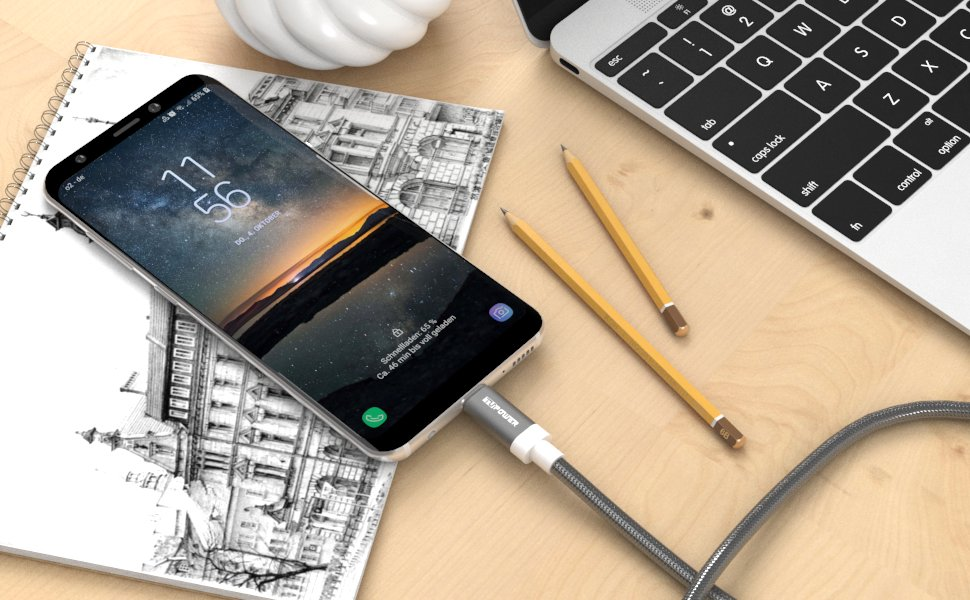 Smartphone auf einem Schreibtisch mit Bleistiften und einem Notizbuch. Ein Ladekabel ist angeschlossen.