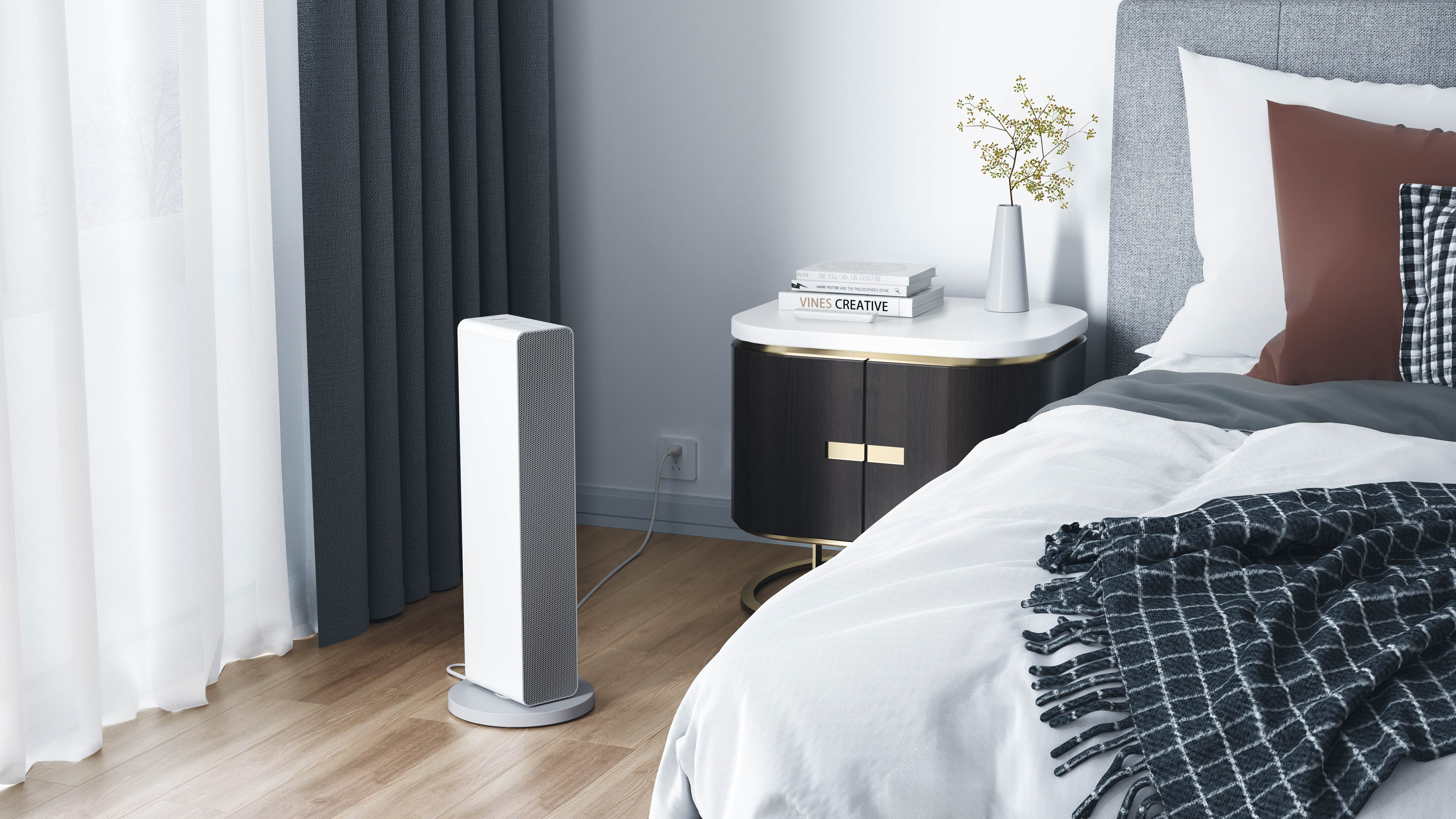 Ein weißer, vertikaler elektrischer Heizkörper steht in einem Raum neben einem Bett und einem Nachttisch.