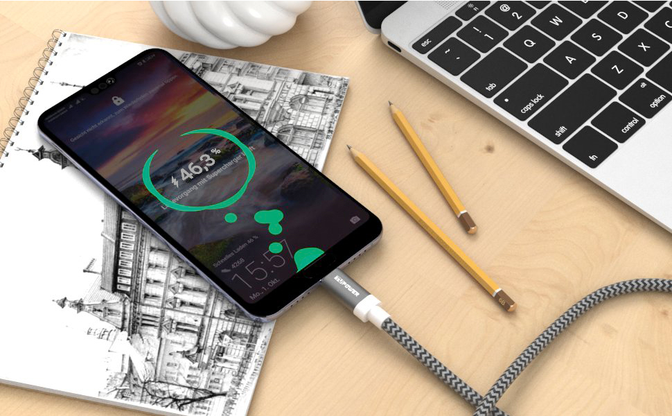 Telefon lädt auf einem Schreibtisch mit Bleistiften und einem Notizbuch. Weißes Kabel. Schwarzes und graues Telefon.