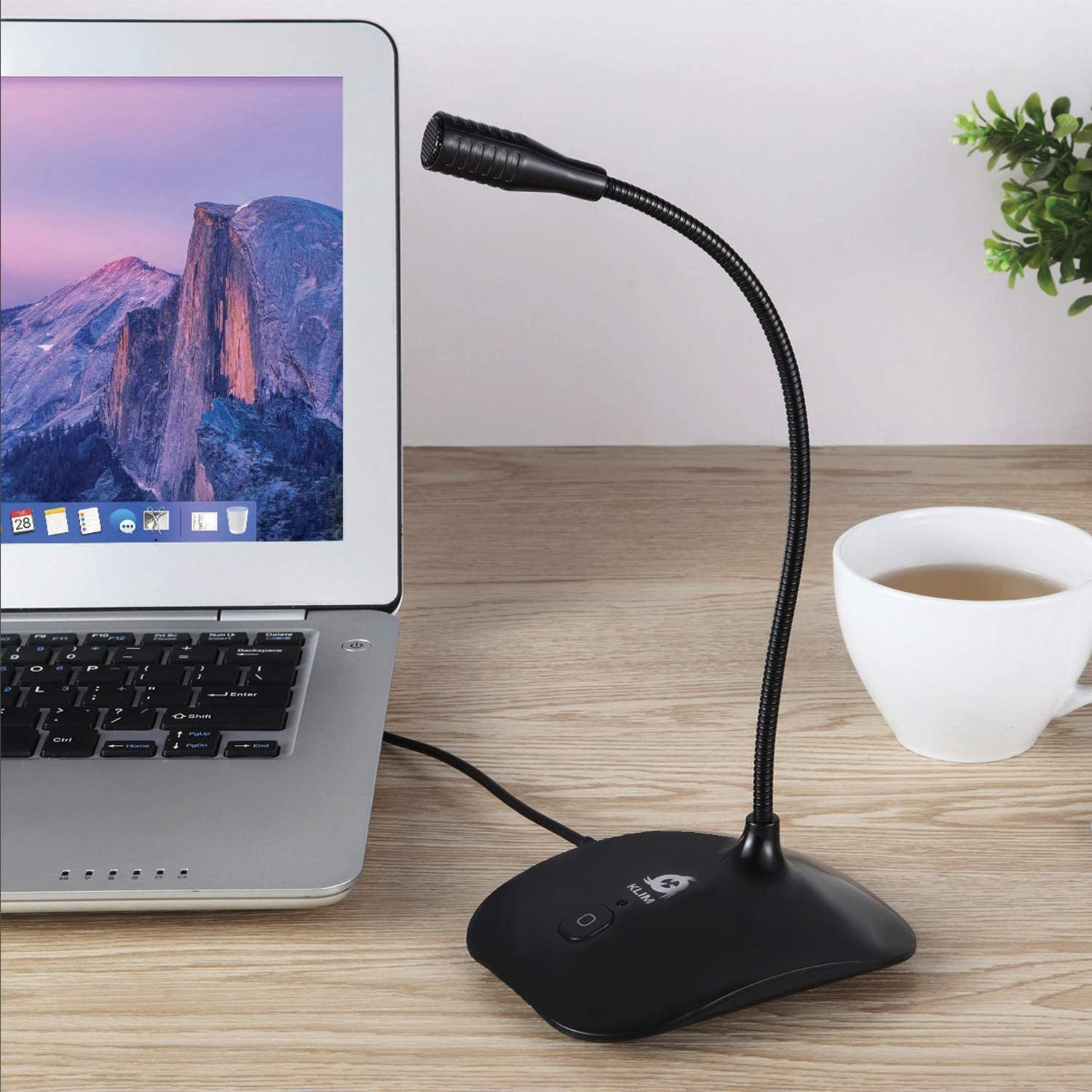 Schwarzes Mikrofon auf einem Schreibtisch mit Laptop und weißer Tasse. Der Hintergrund zeigt einen Berg.