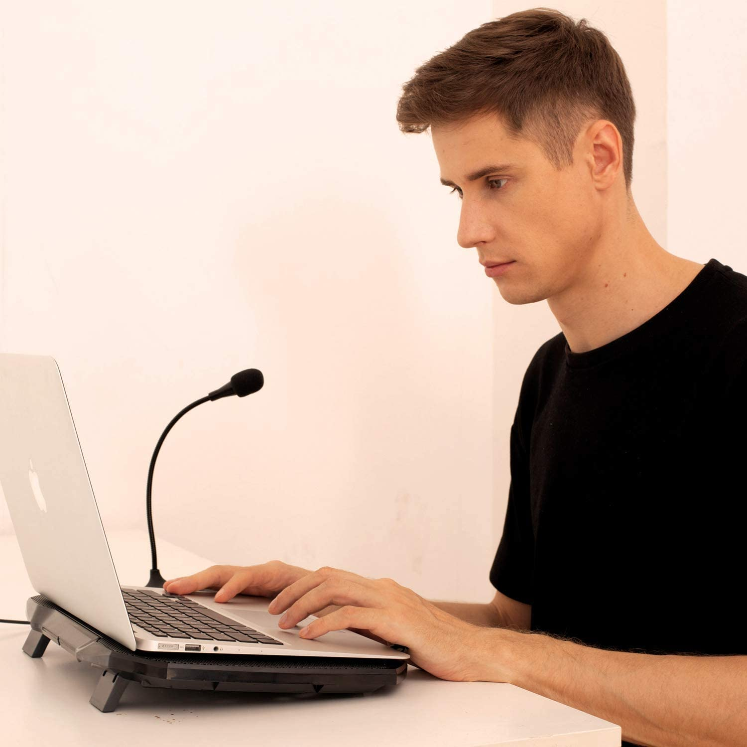 Ein Mann arbeitet an einem Laptop mit Mikrofon, sitzend an einem weißen Schreibtisch.