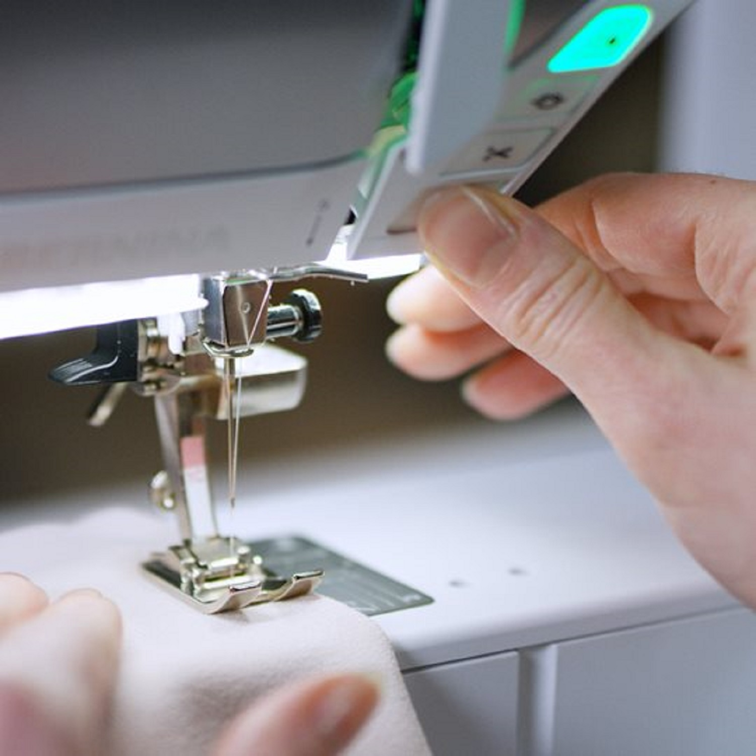 Nahaufnahme einer Nähmaschine, mit einer Hand, die ein Bedienfeld mit beleuchteter Taste einstellt.