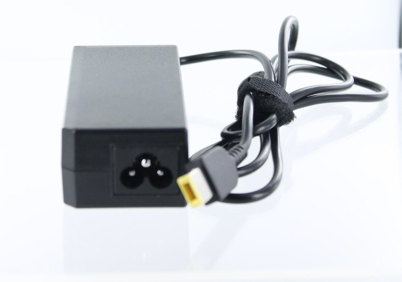 Schwarzes Netzteil mit einem dreipoligen Stecker. Schwarzes Kabel. Weißer Hintergrund.