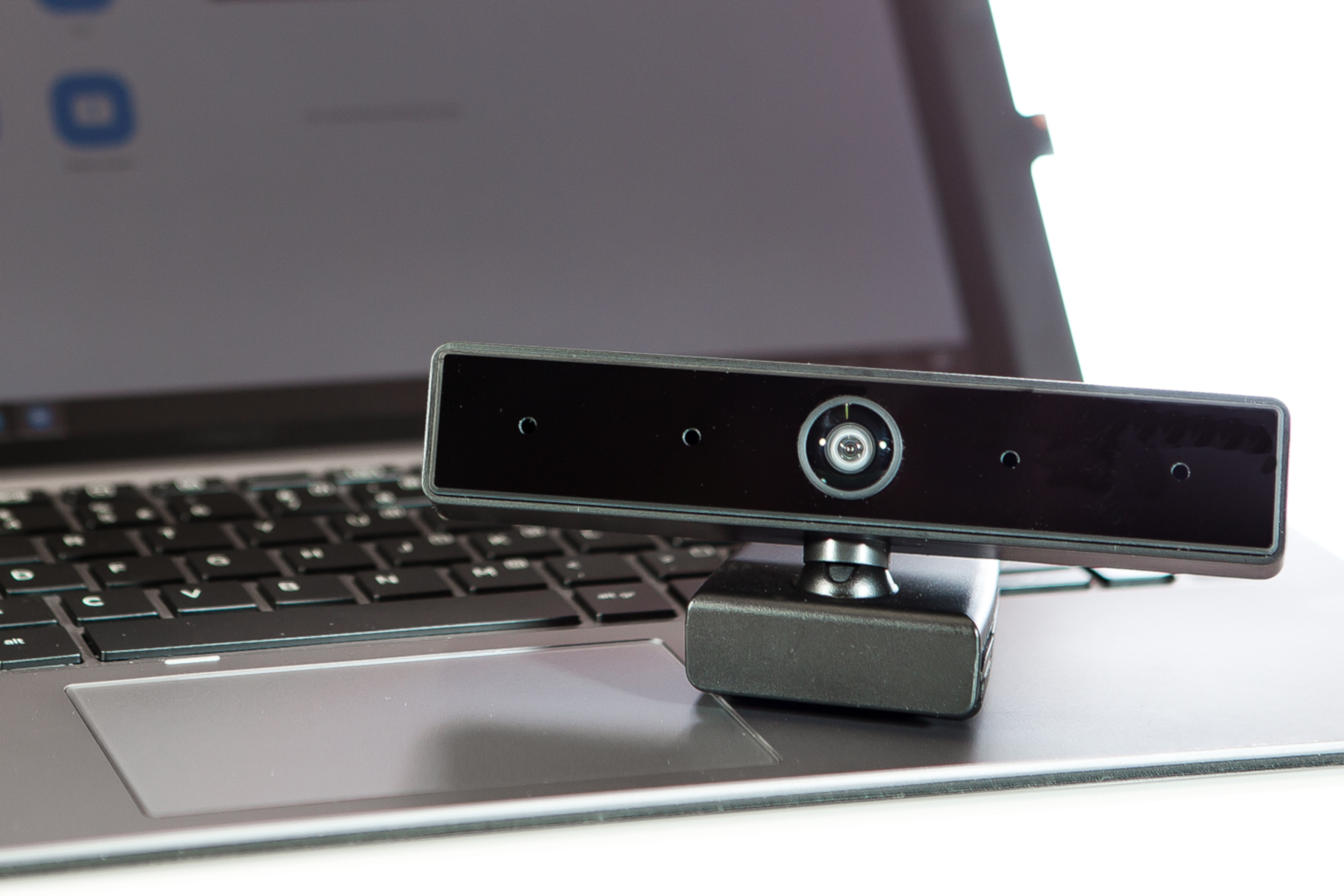 Eine schwarze Webcam sitzt auf einem Laptop, der Bildschirm zeigt eine Website, auf weißem Hintergrund.