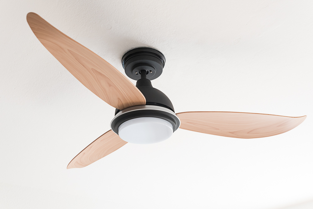 Ein Deckenventilator mit drei Holzflügeln und einem weißen Licht, montiert an einer weißen Decke.