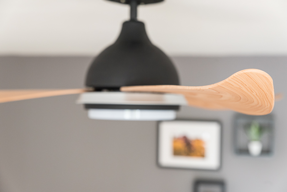 Ein Deckenventilator mit Holzblättern und einem schwarzen Motor. Im Hintergrund ist ein verschwommenes Interieur.
