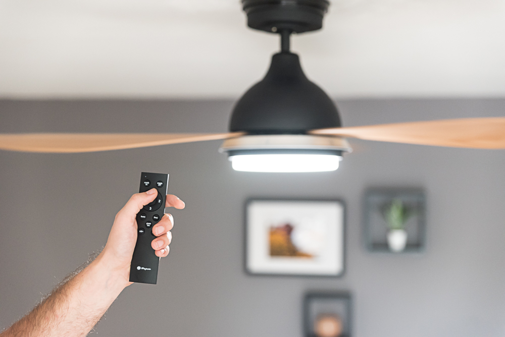 Eine Hand hält eine Fernbedienung und zielt auf einen Deckenventilator mit Licht.