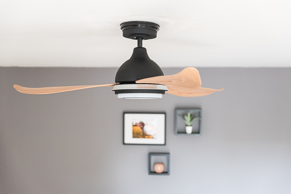 Deckenventilator, schwarzer Motor, Holzblätter, Deko im Hintergrund.