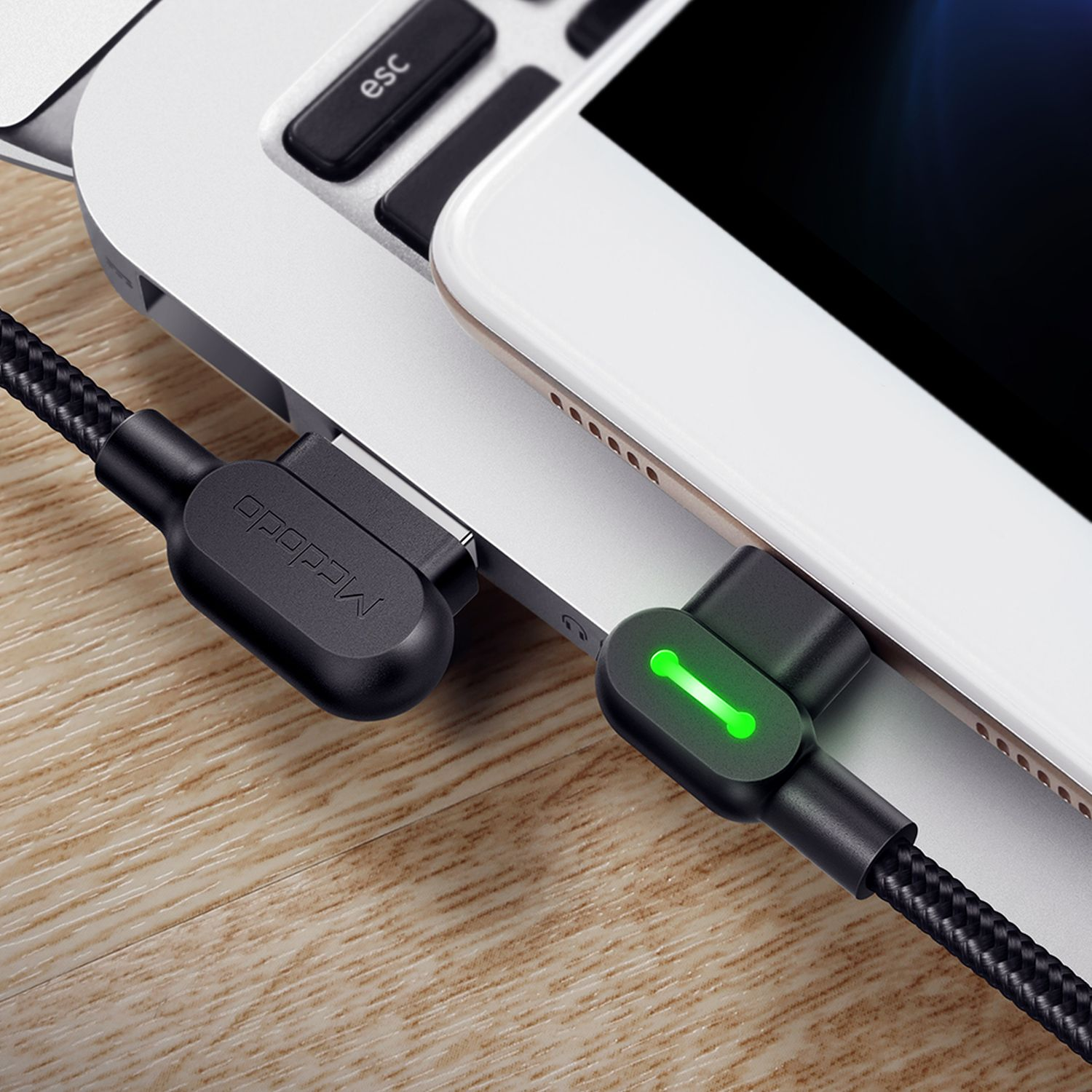 Schwarzes Ladekabel an Laptop und Telefon angeschlossen, grünes Licht.