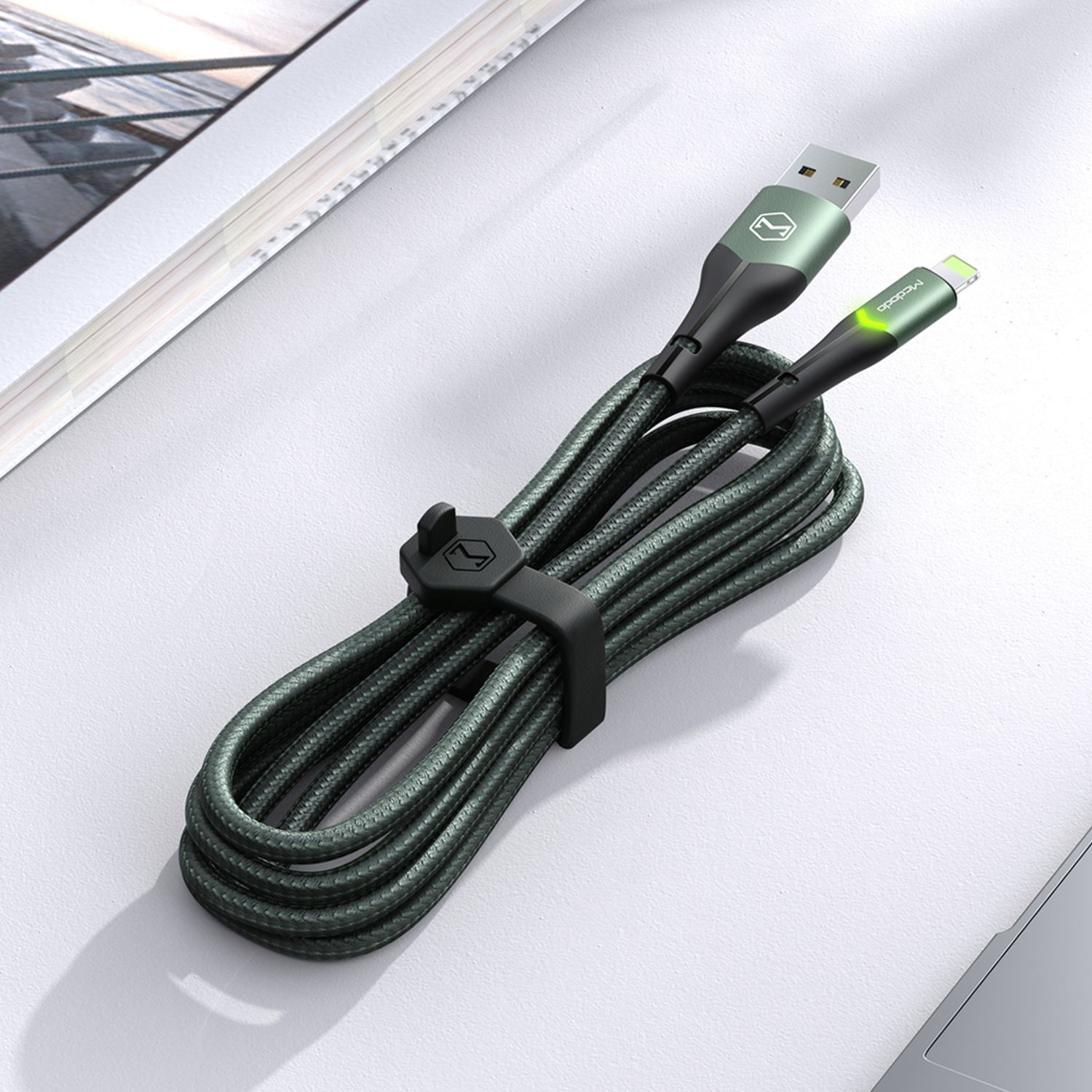 Ein grün-schwarzes USB-C-Kabel, mit schwarzem Riemen auf einem Schreibtisch.