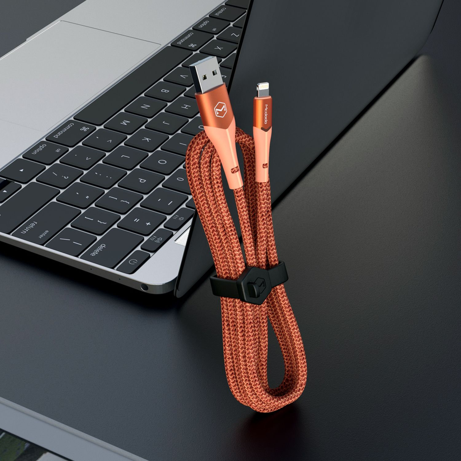 Siyah kablo bağı ile turuncu USB-C kablosu, bir dizüstü bilgisayarın yanında.