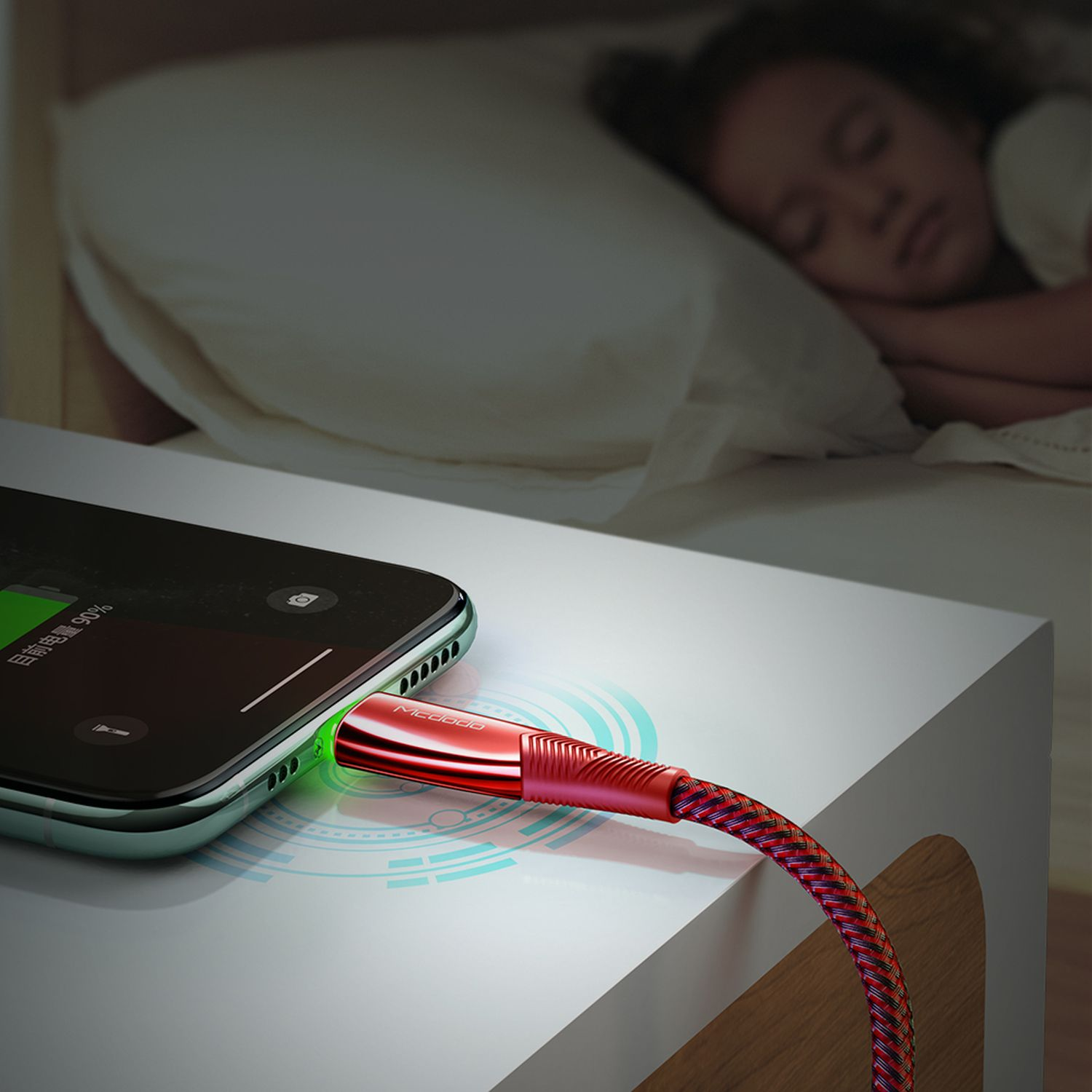 Ein Telefon, das auf einem weißen Nachttisch aufgeladen wird, mit einem roten Ladekabel verbunden.