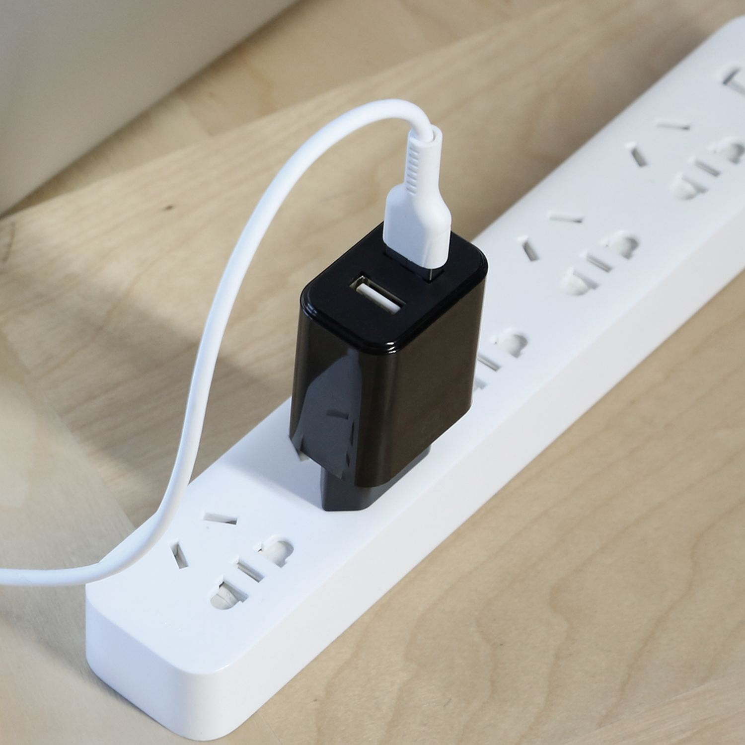 Schwarzes USB-Ladegerät an einer weißen Steckdosenleiste. Weißes Kabel am Ladegerät.