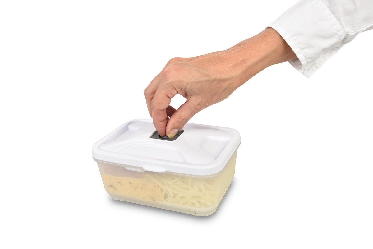 Eine Hand legt einen grünen Gegenstand in einen weißen Behälter mit Pasta.