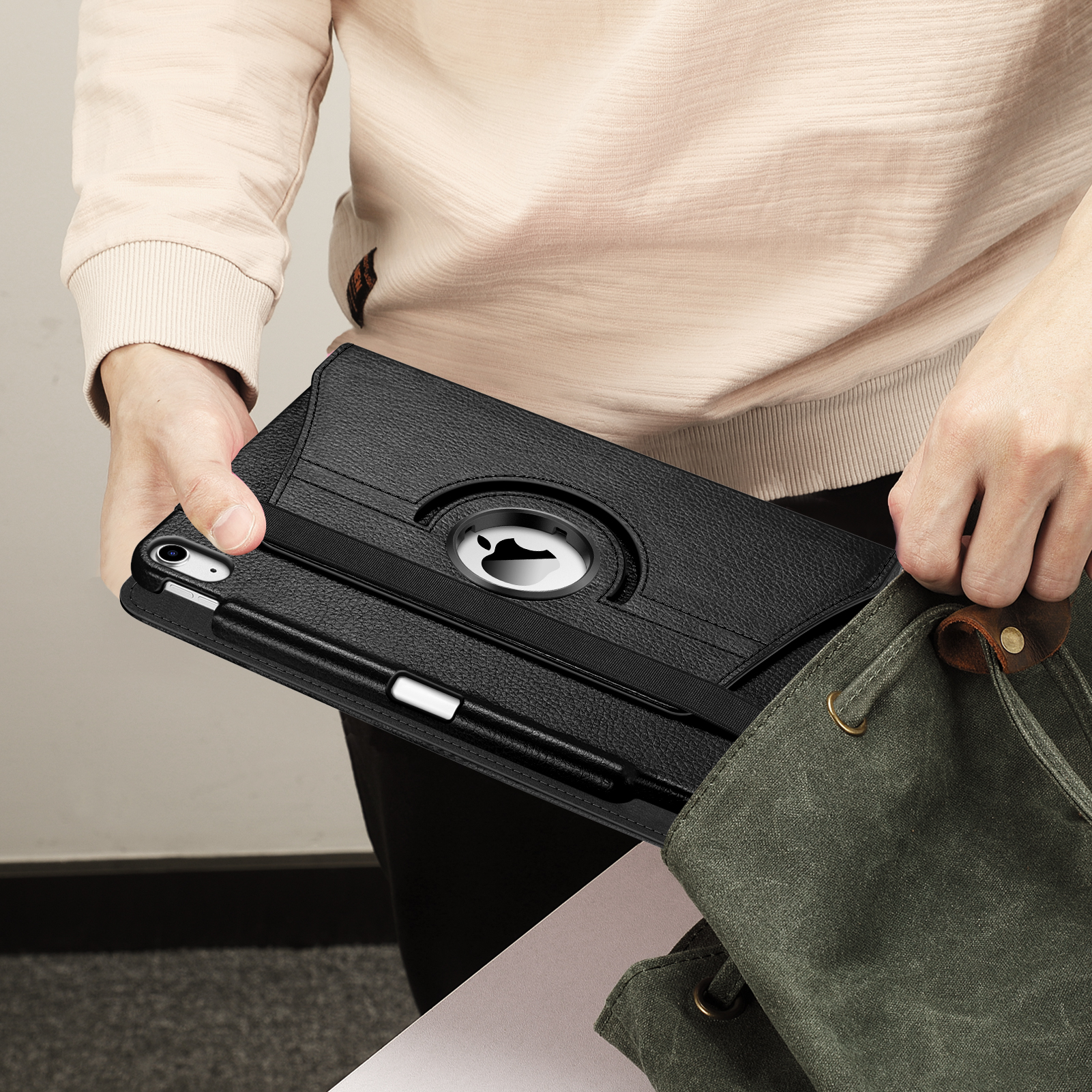 Person hält eine schwarze iPad-Hülle mit Apple-Logo und legt sie in eine grüne Tasche.