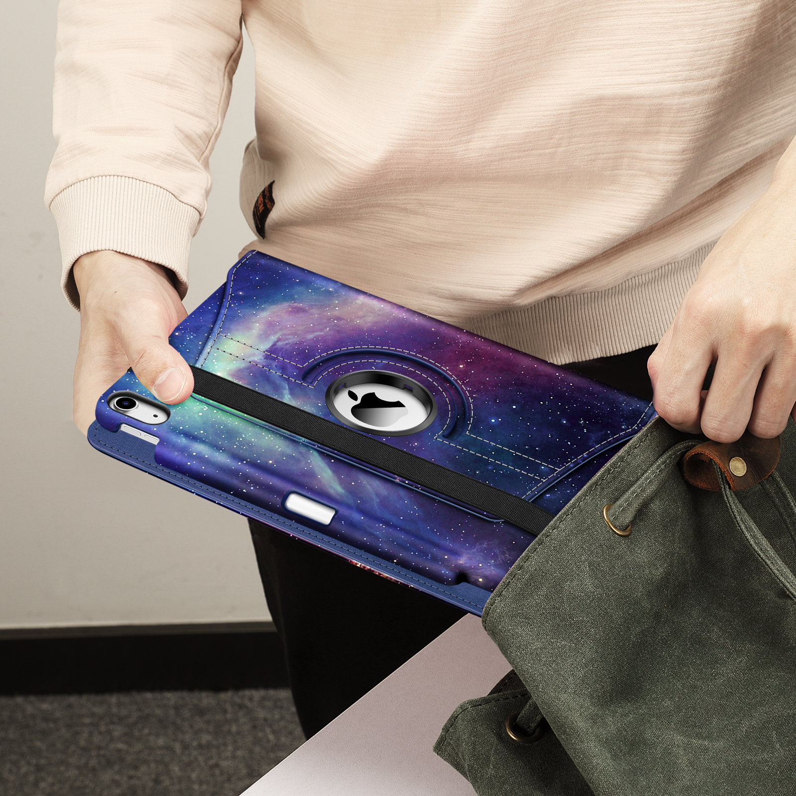 Eine Person hält ein Tablet in einer Hülle mit Galaxiemotiv, Hände vor einer grünen Tasche.