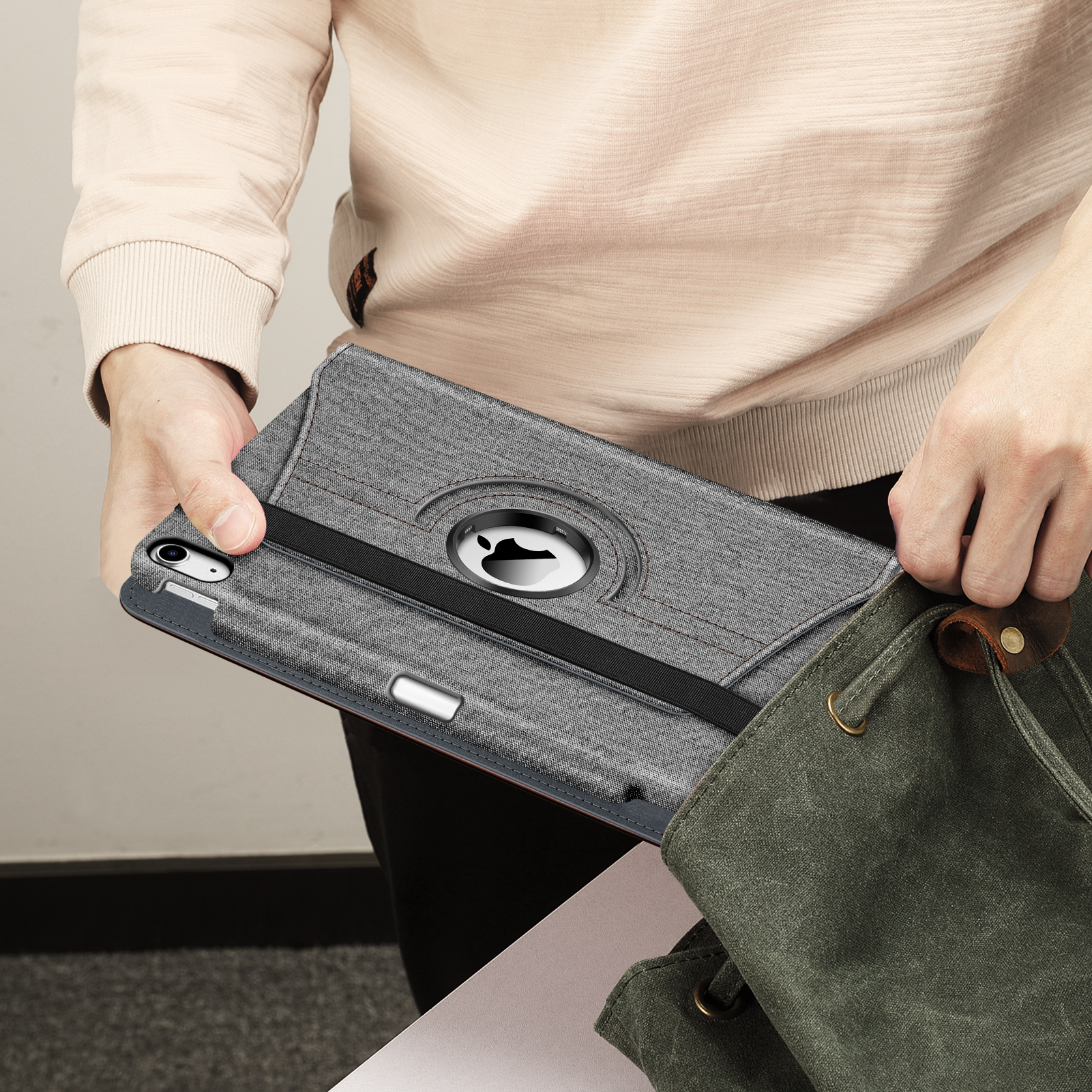 Person hält graue Tablethülle und steckt sie in eine grüne Canvas-Tasche.