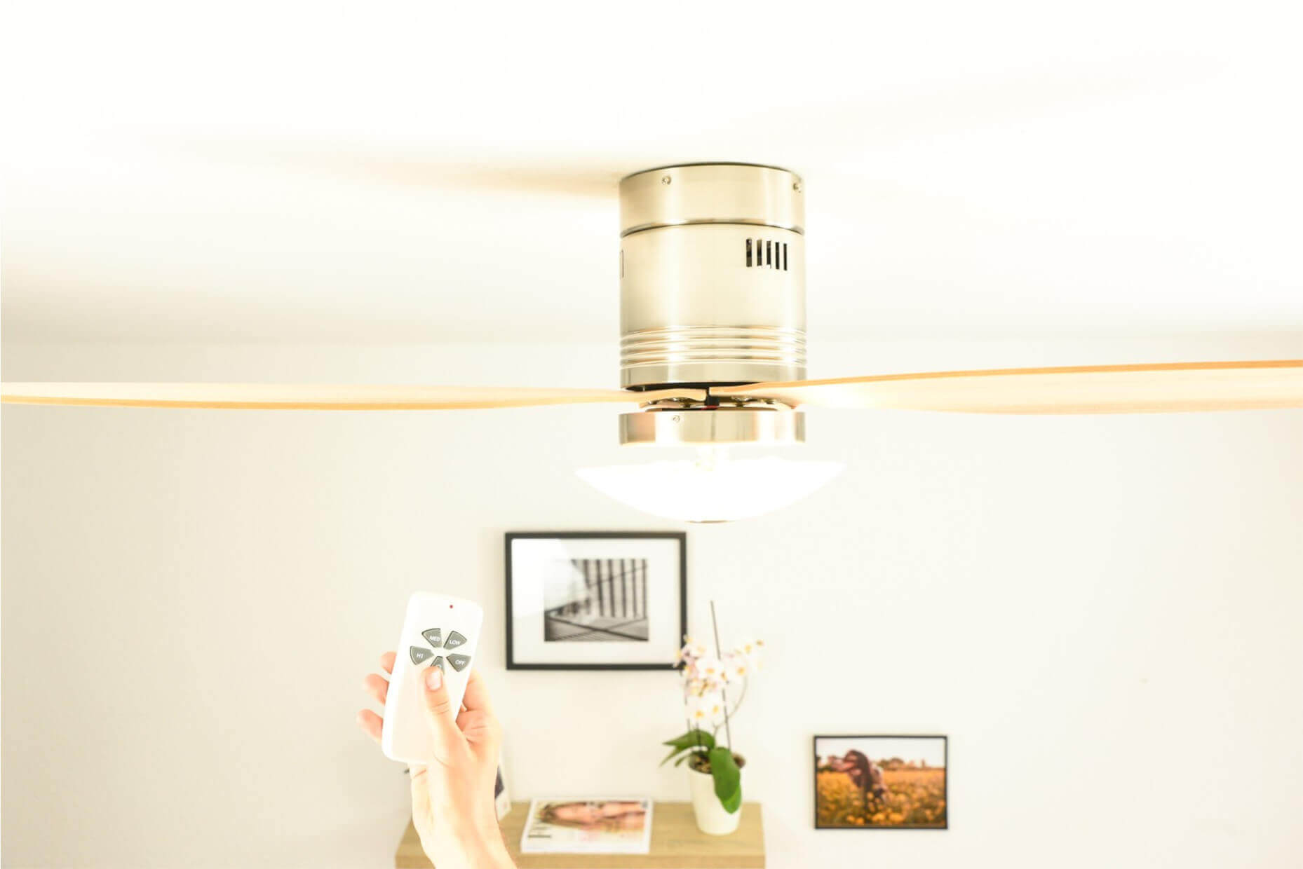 Eine Hand hält eine Fernbedienung, die auf einen Deckenventilator mit Licht zeigt.