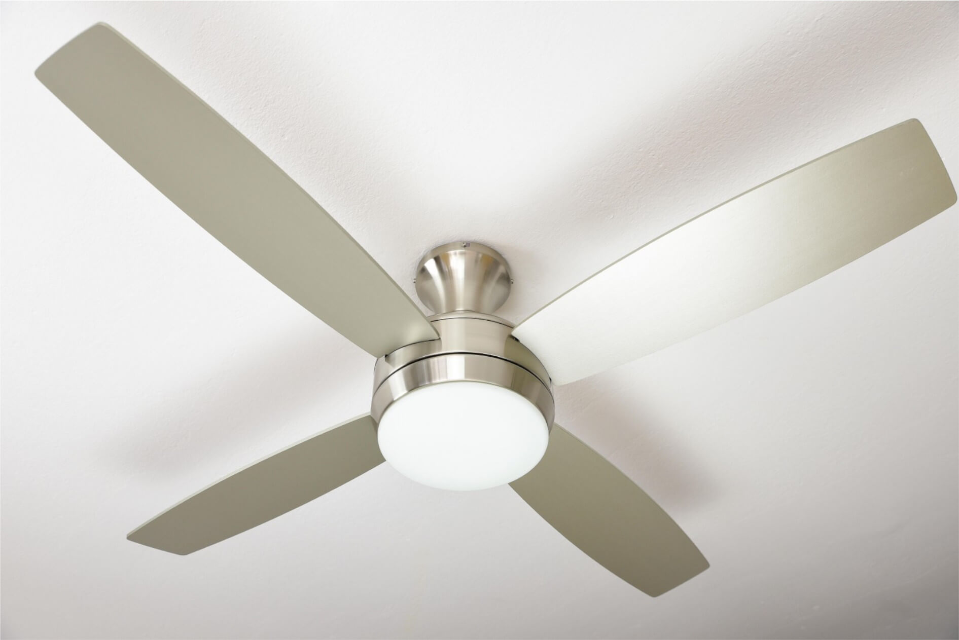 Un ventilatore a soffitto con quattro pale e una luce. Il ventilatore è argento e bianco, montato su un soffitto bianco.