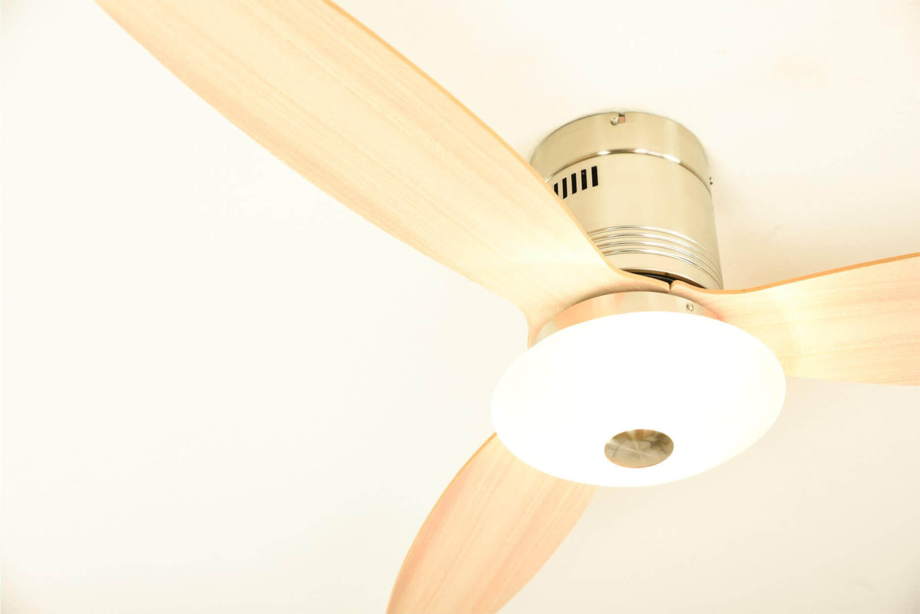 Deckenventilator mit drei hellfarbigen Flügeln und einer zentralen Leuchte, vor weißem Hintergrund.