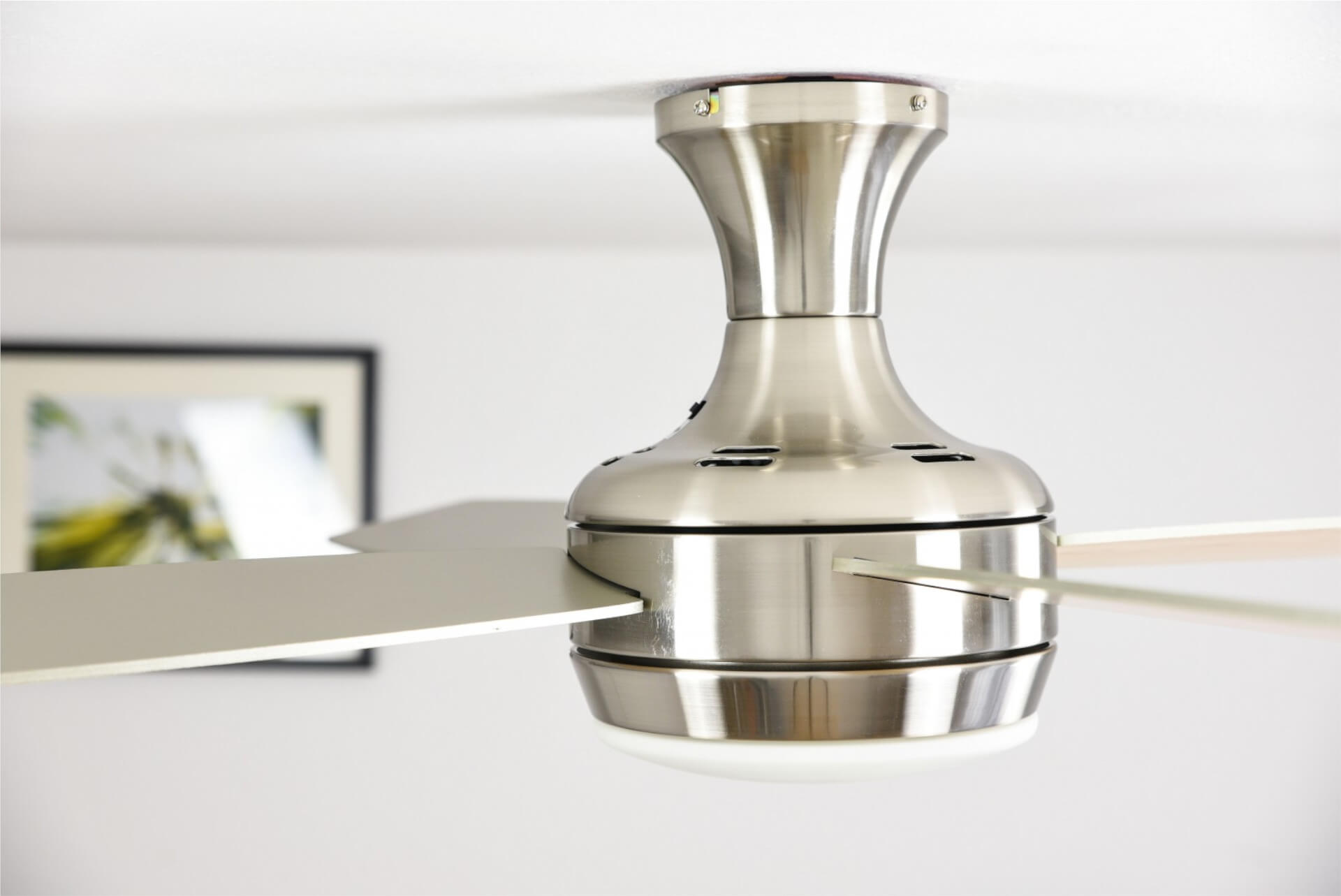 Ventilatore da soffitto con corpo e pale argentate. Fissato al soffitto bianco.