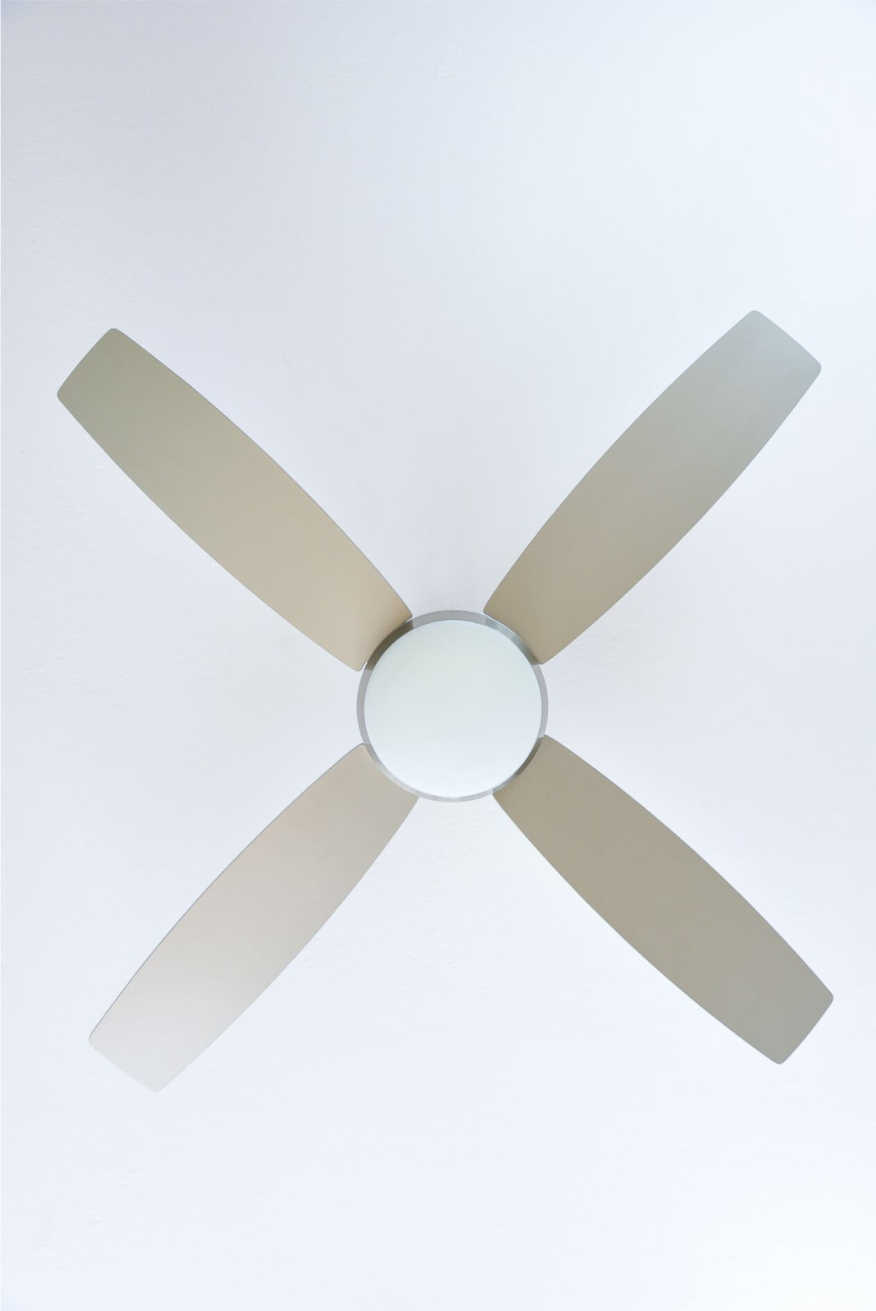 Ventilatore da soffitto visto dal basso. Quattro pale beige con luce centrale. Sfondo bianco.