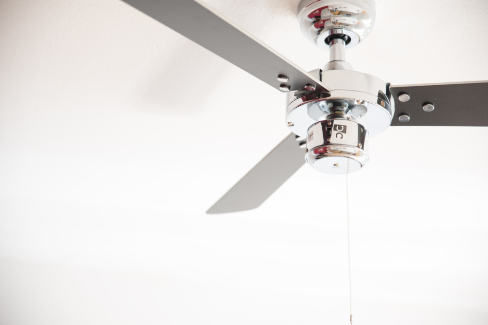 Deckenventilator mit silbernen und grauen Flügeln. Weiße Decke im Hintergrund.