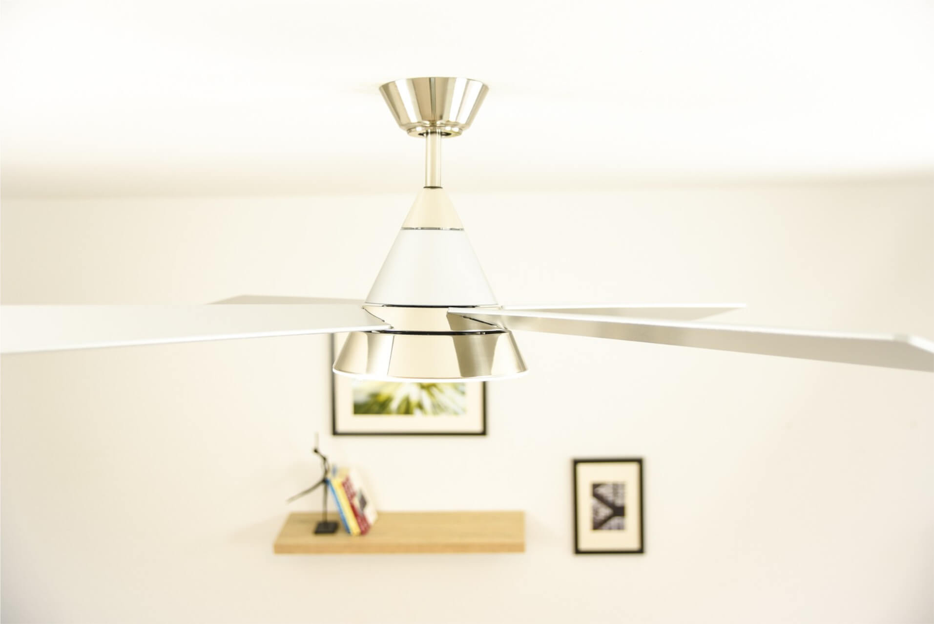 Ventilatore da soffitto con pale bianche, finiture cromate e soffitto bianco.