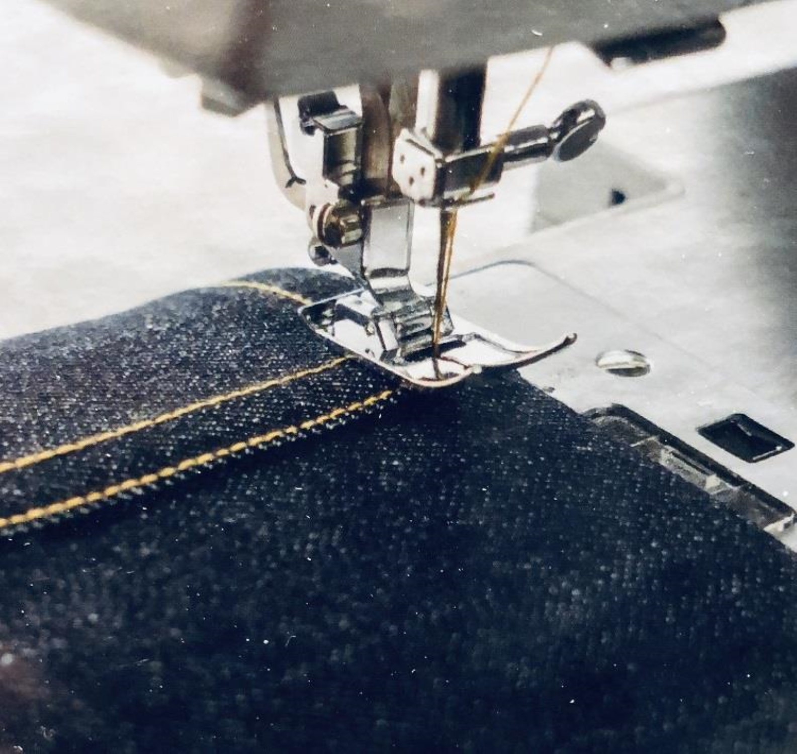 Igła maszyny do szycia przebija ciemnoniebieski dżins z żółtą nicią.