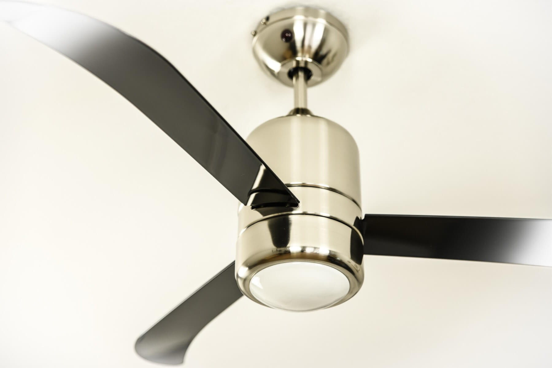 Deckenventilator mit schwarzen Flügeln und silbernem Motor und Sockel. Die Flügel sind abgewinkelt.