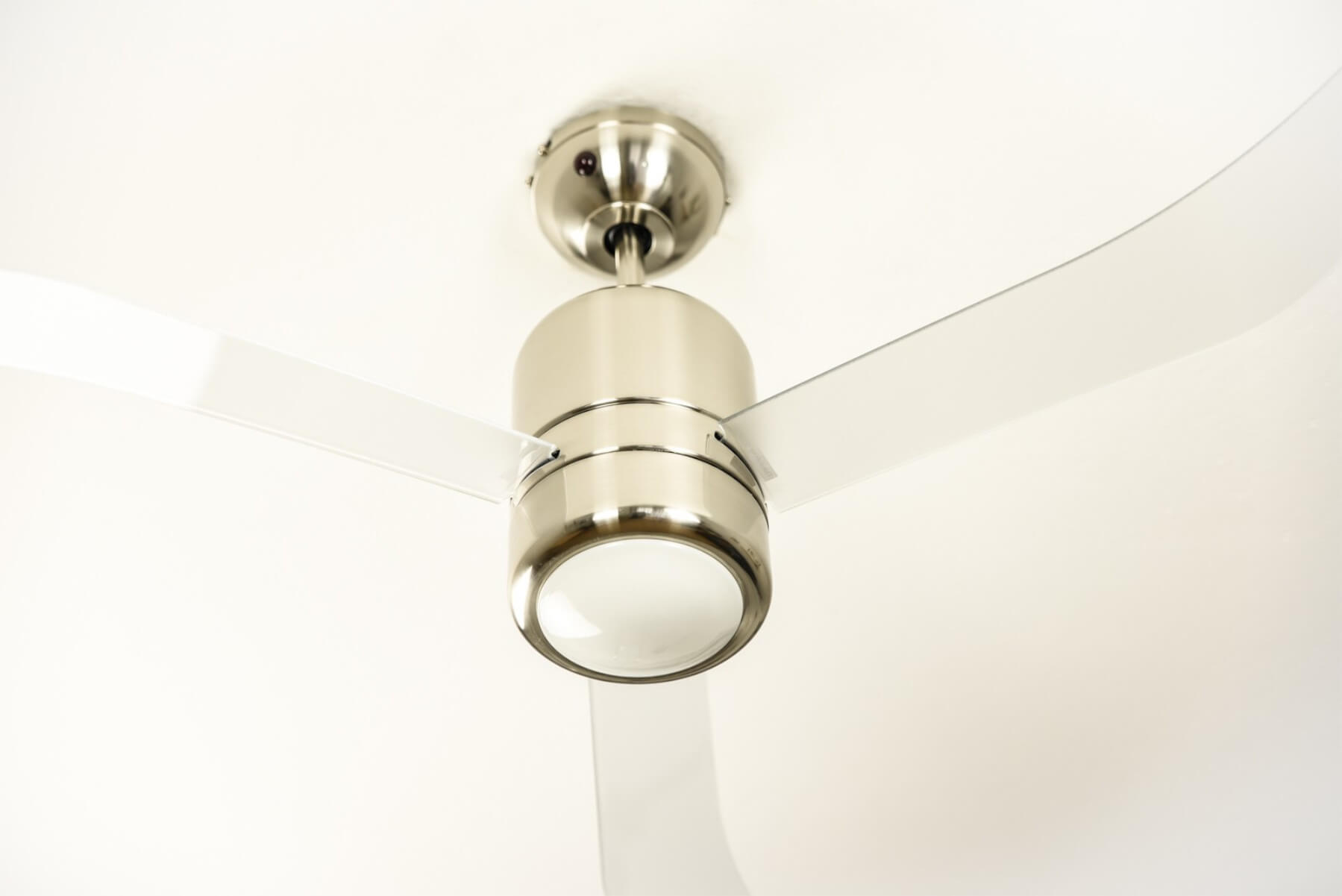 Deckenventilator mit drei weißen Flügeln. Silbernes Motorgehäuse und weiße Decke.