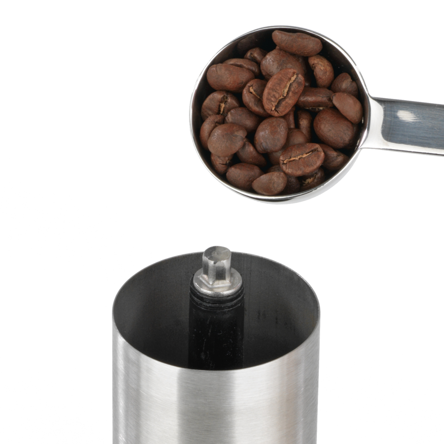Kaffeebohnen in einem Messlöffel über einer Mühle.