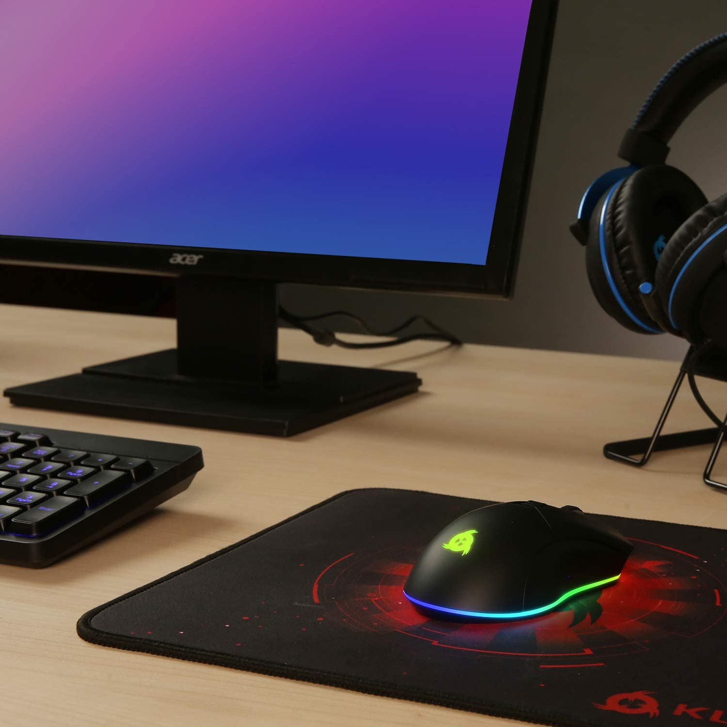 Ein Computer-Setup mit Monitor, Tastatur, Maus und Kopfhörern auf einem Holzschreibtisch.